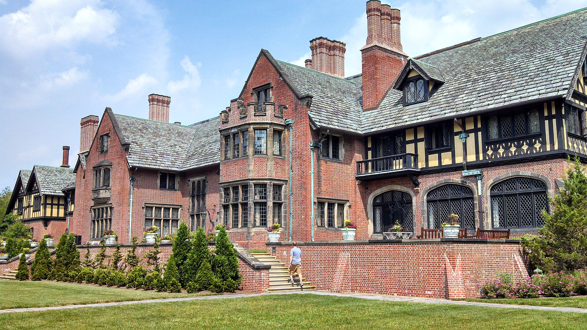 Stan Hywet Hall's Tudor Revival brick manor and green lawn in Akron on a sunny day.