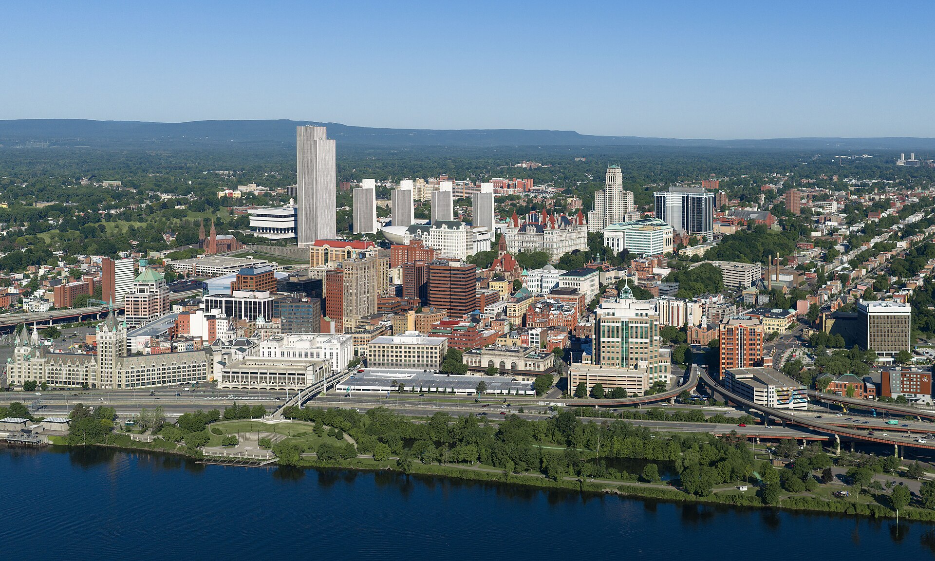 Downtown Albany's skyline, with the Empire State Plaza towers and the Capitol, rising above the Hudson River on a clear day.