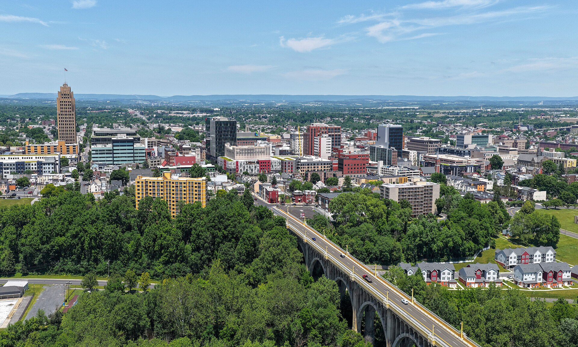 Downtown Allentown’s skyline with the Art Deco PPL Building and the arched Eighth Street Bridge above green parkland on a sunny day.
