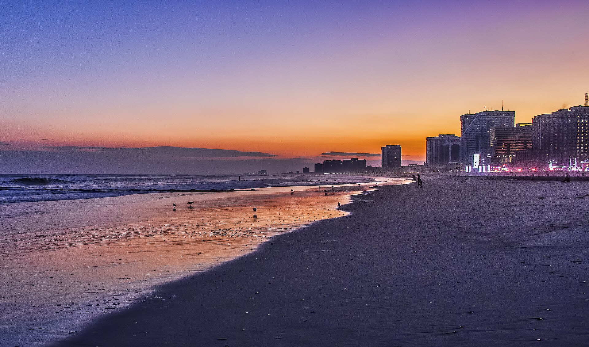 The beach and surf at sunset with Atlantic City's lit casino towers along the shore.