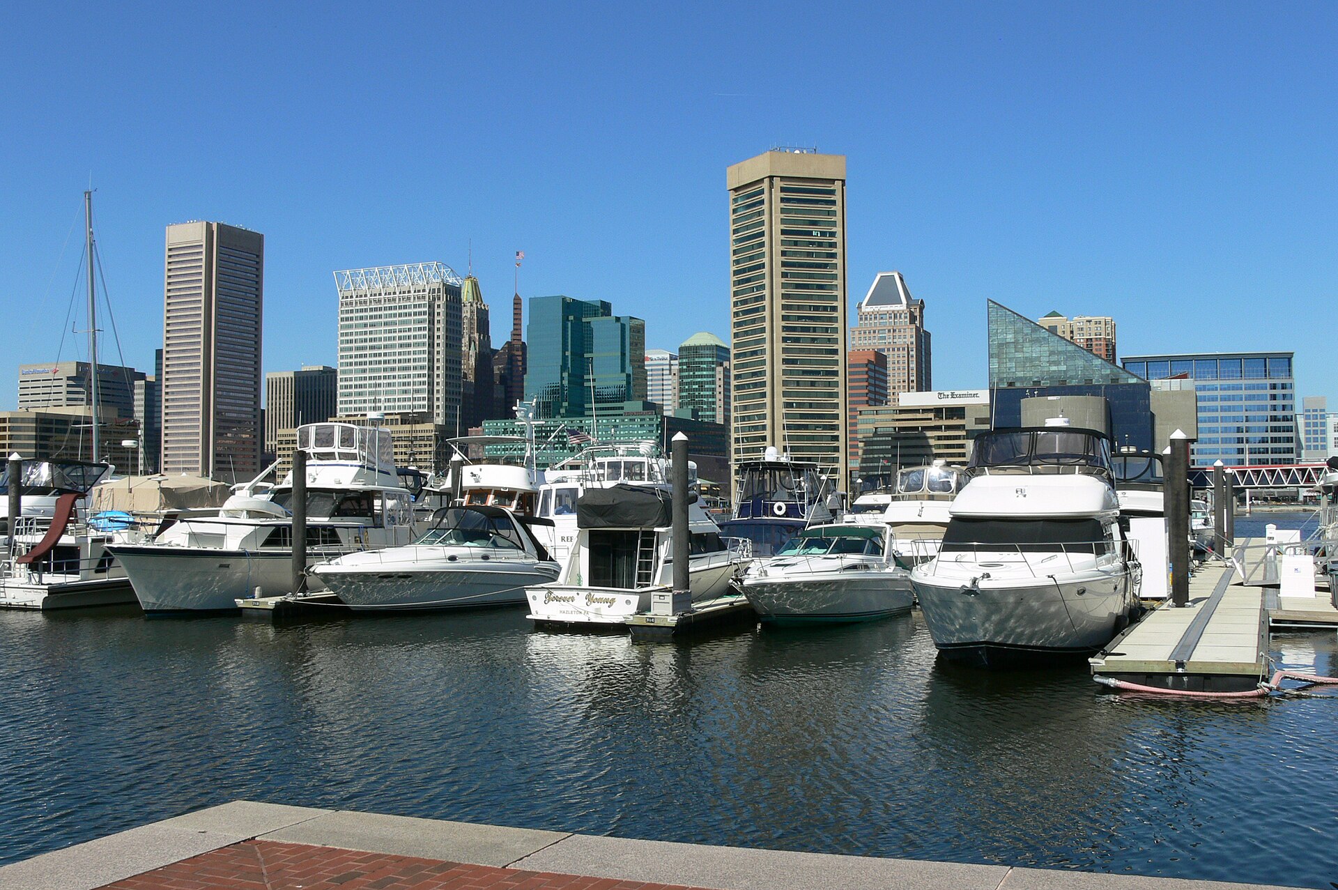 Boats moored in Baltimore's Inner Harbor below the downtown skyline on a clear, sunny day.
