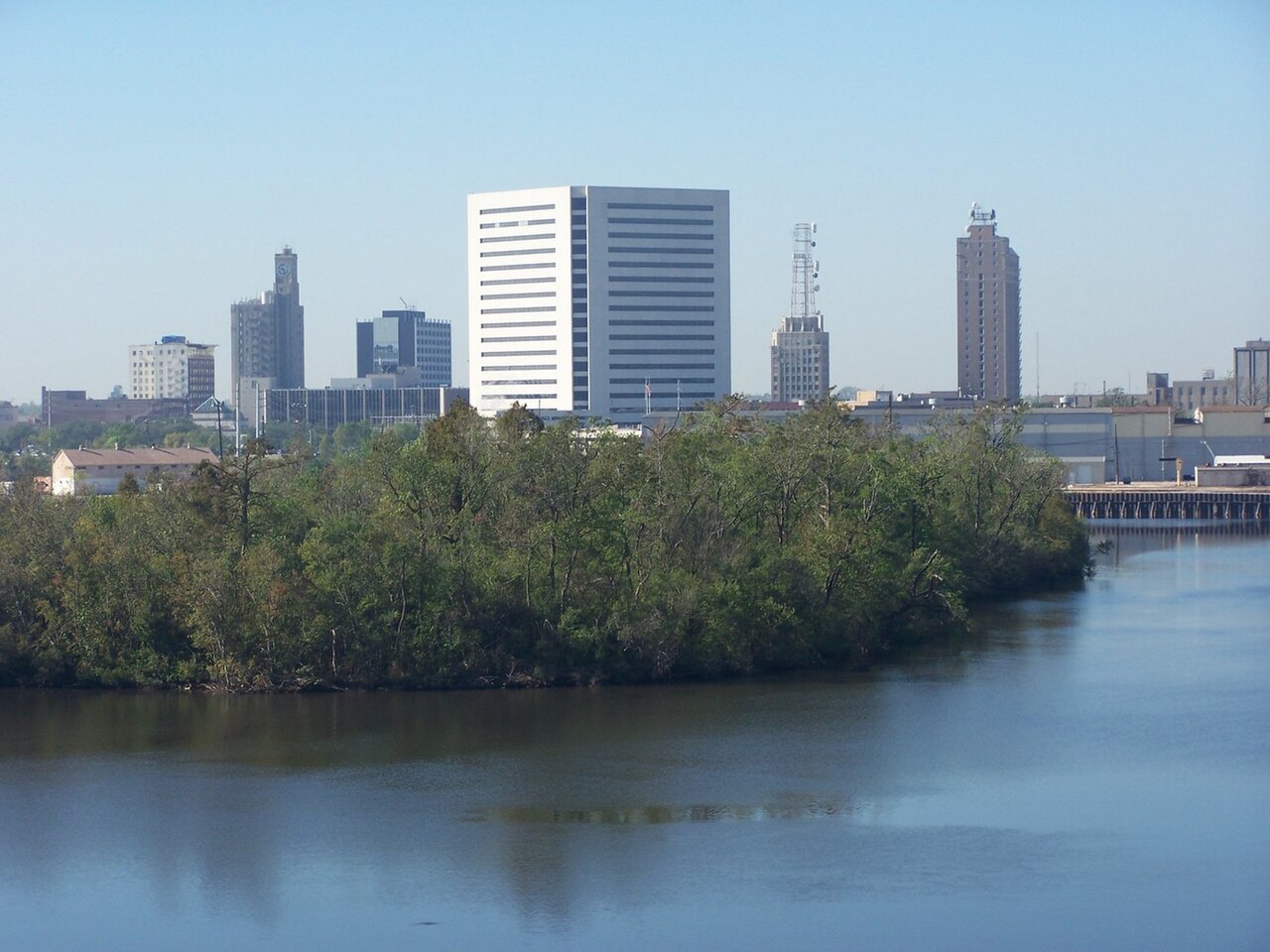 Downtown Beaumont towers rising beyond the tree-lined Neches River on a clear day.