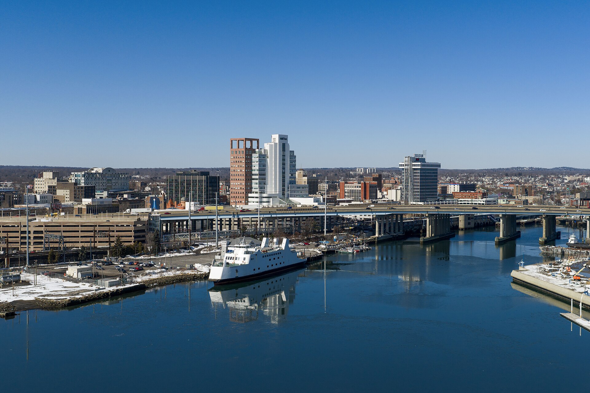 Downtown Bridgeport's towers across the harbor, with a ferry at its dock in the foreground, on a clear winter day.