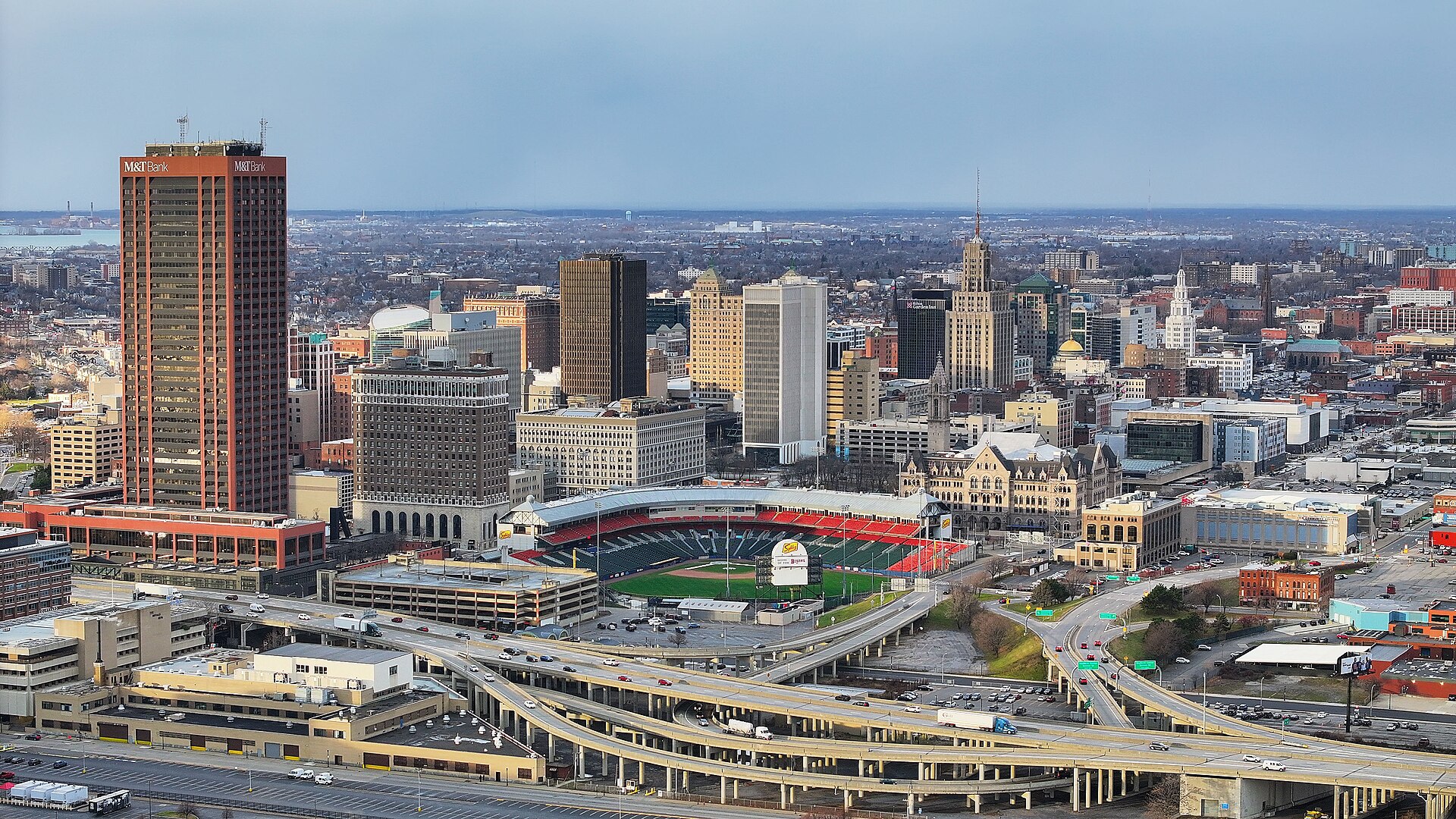 Downtown Buffalo skyline and Sahlen Field ballpark in late-afternoon light, seen from above the waterfront.