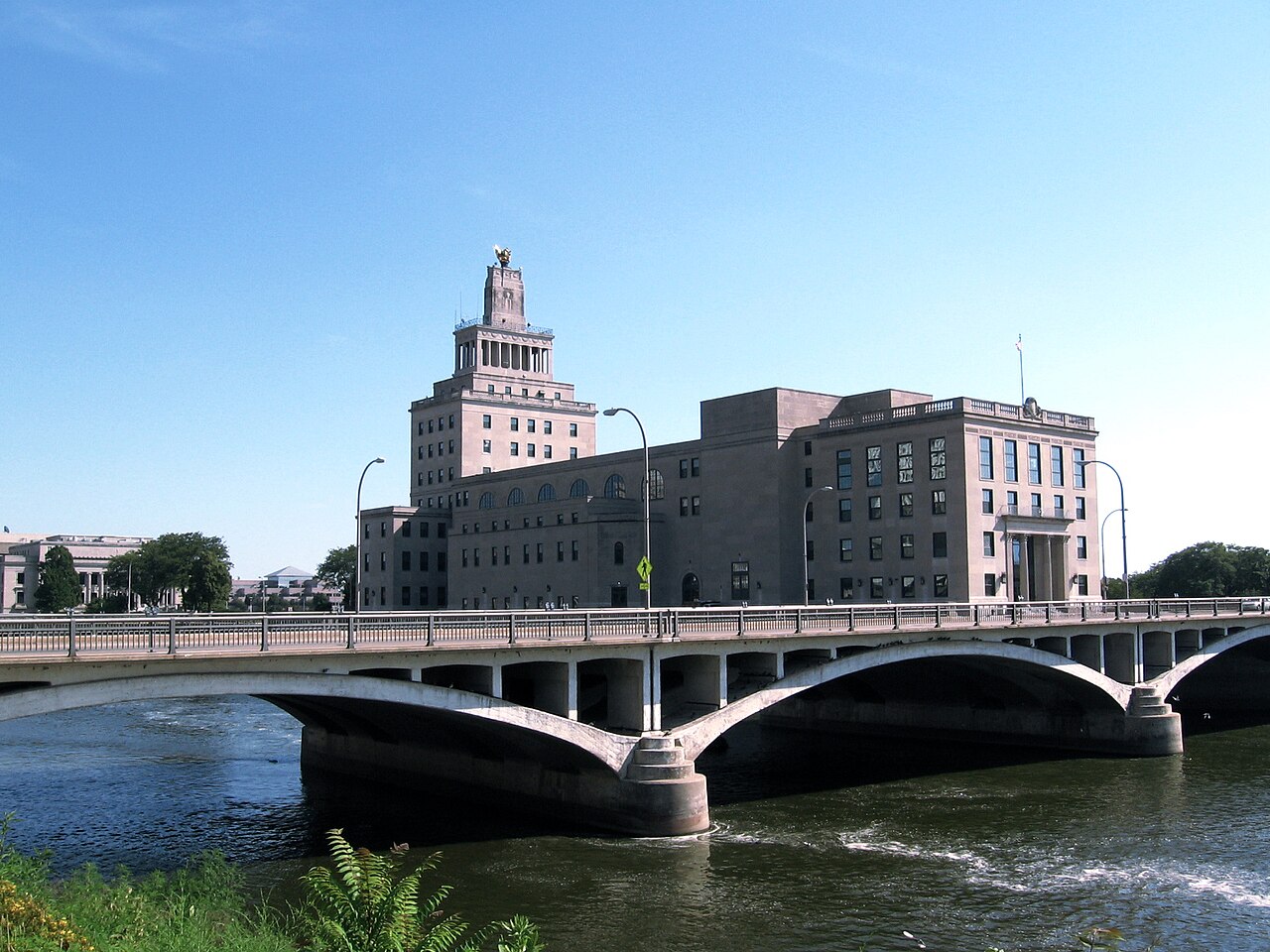 The Veterans Memorial Building on Mays Island in Cedar Rapids, beside an arched bridge over the Cedar River.