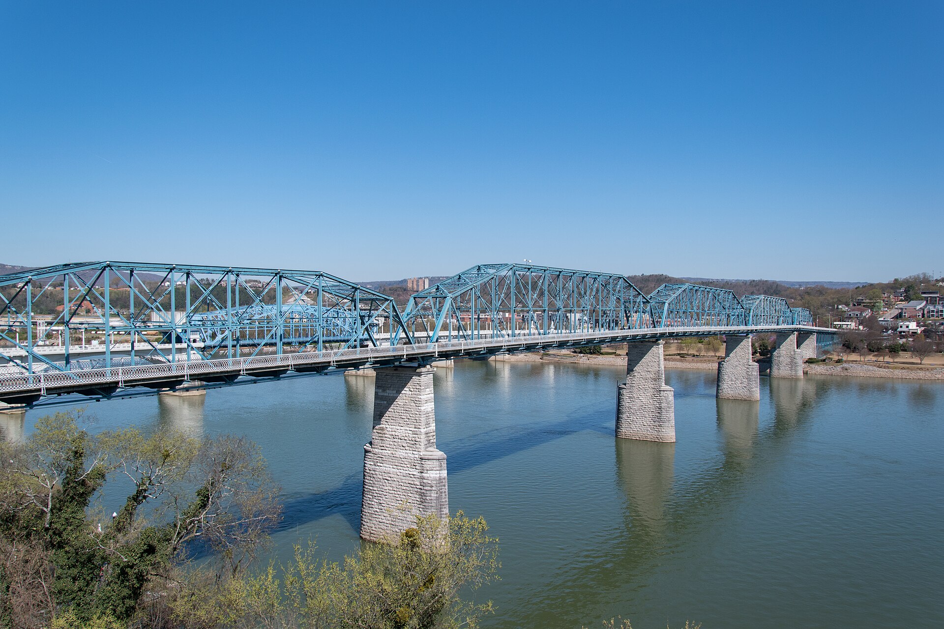 The blue Walnut Street pedestrian bridge spanning the Tennessee River in Chattanooga under a clear blue sky.