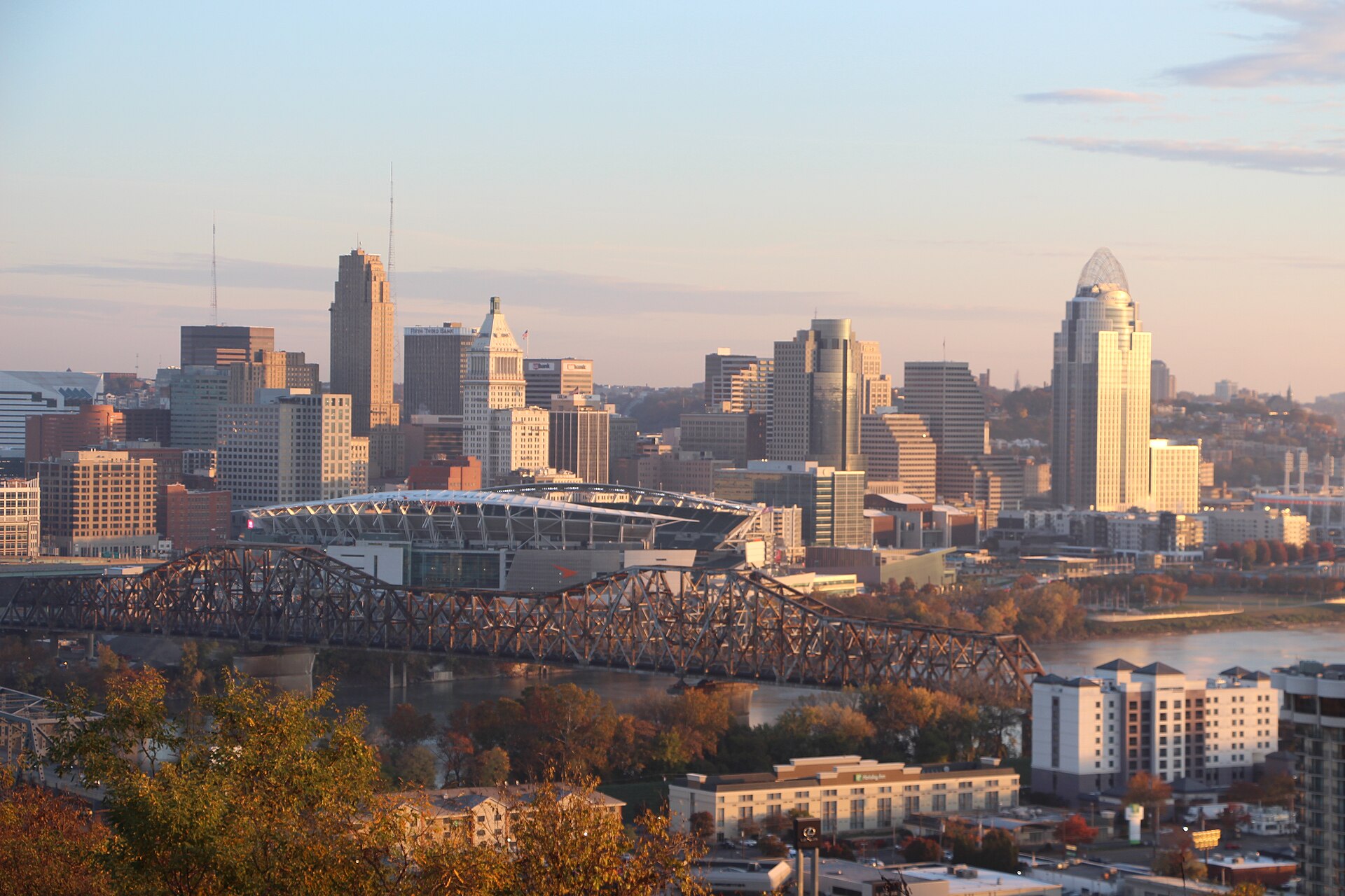 Downtown Cincinnati skyline and an Ohio River bridge in warm late-afternoon light, seen from Devou Park across the river.
