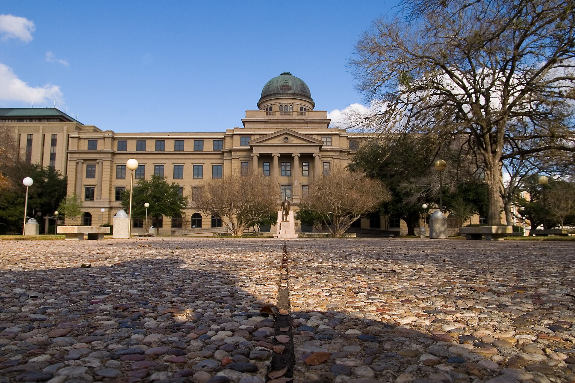 The domed Academic Building at Texas A&M University in College Station under a blue sky, seen across the plaza.