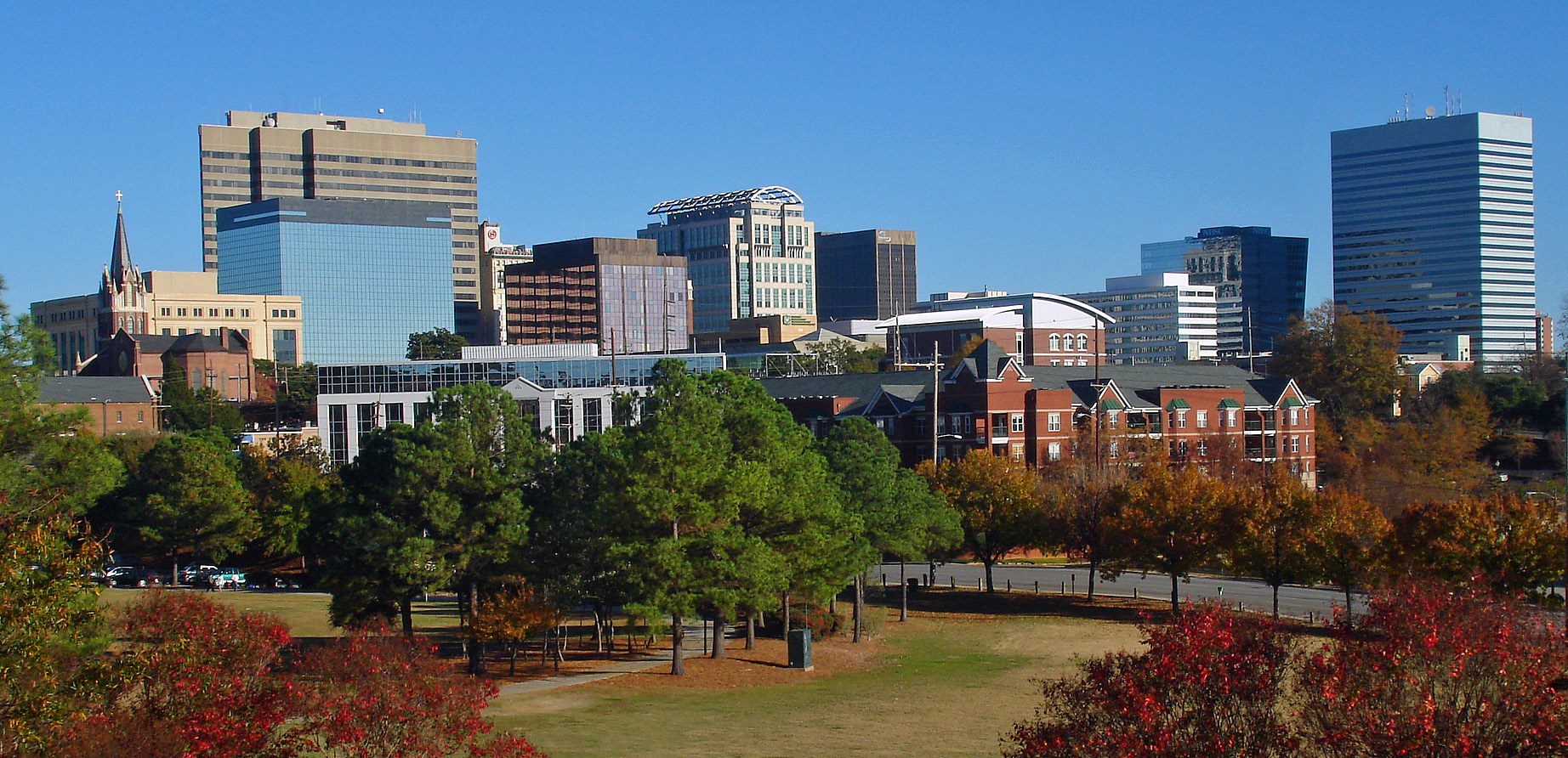 Downtown Columbia's office towers rise above autumn trees, seen from Arsenal Hill under a clear blue sky.