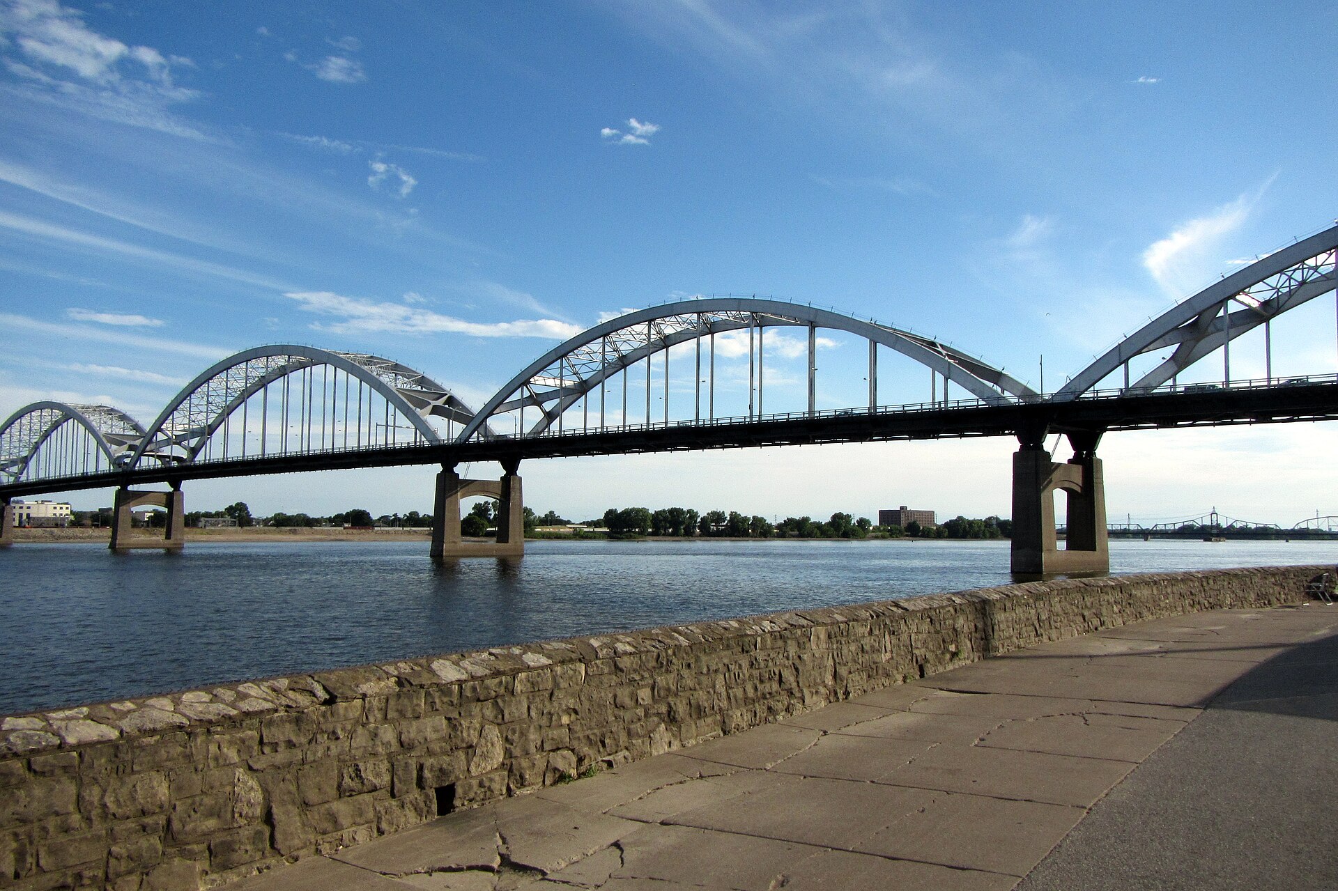 The arches of the Centennial Bridge spanning the Mississippi River at Davenport, seen from the riverside wall on a sunny day.