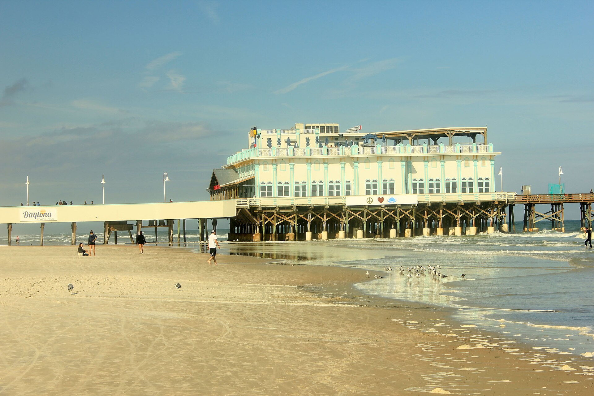 The Main Street Pier and its pier-top restaurant stretching over the sand and surf at Daytona Beach on a sunny afternoon.
