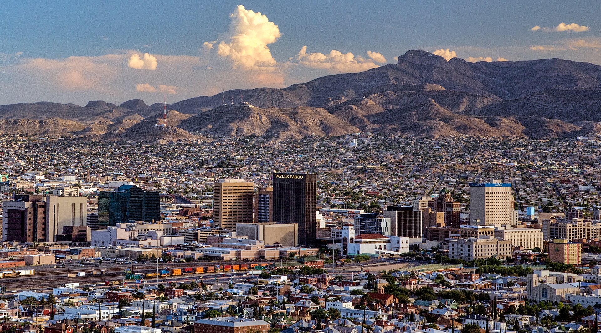 Downtown El Paso’s high-rises, with Ciudad Juárez and rugged mountains beyond, seen from Scenic Drive under a blue sky.