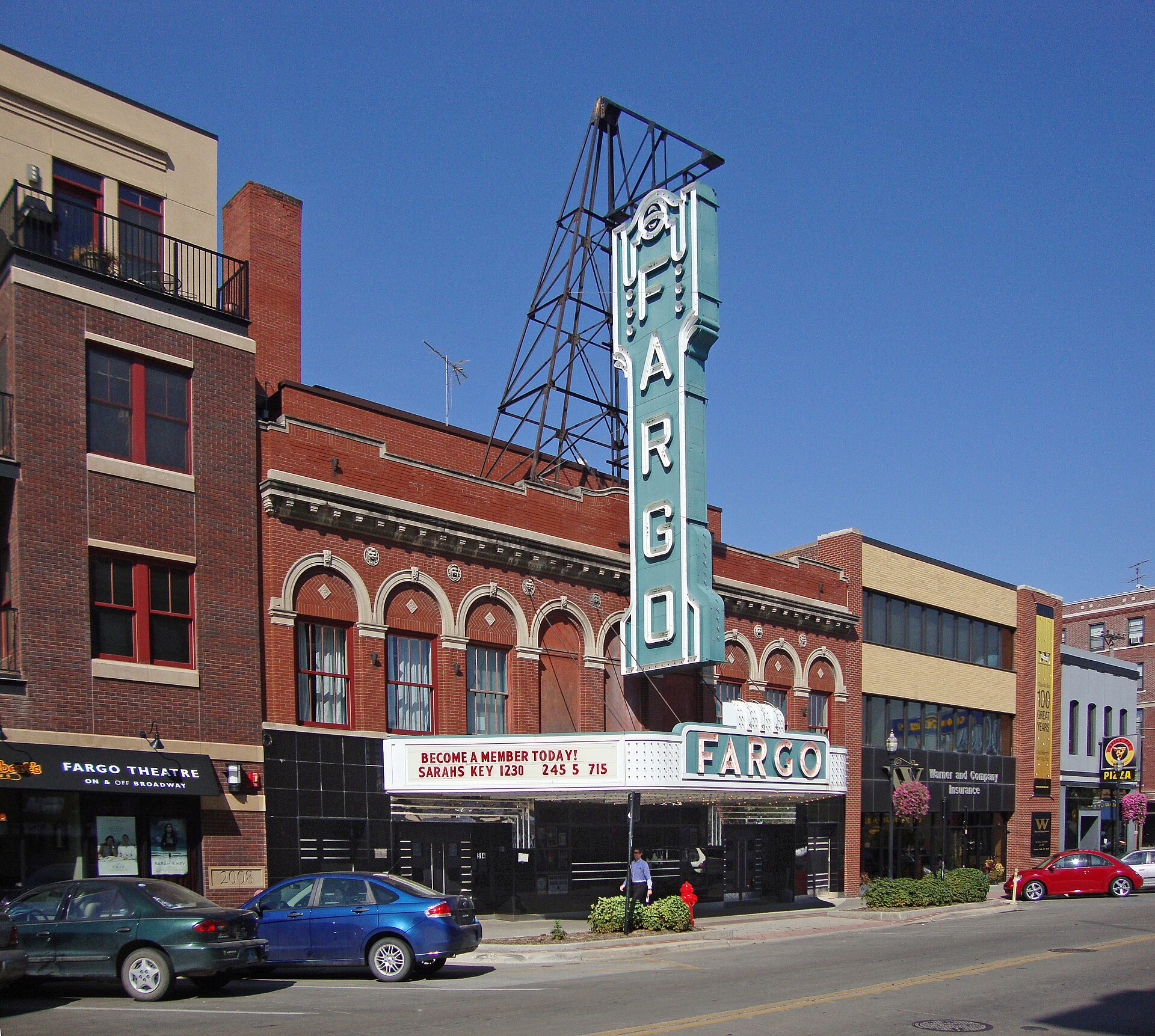 The Fargo Theatre with its tall vertical FARGO sign and marquee on Broadway in downtown Fargo on a sunny day.