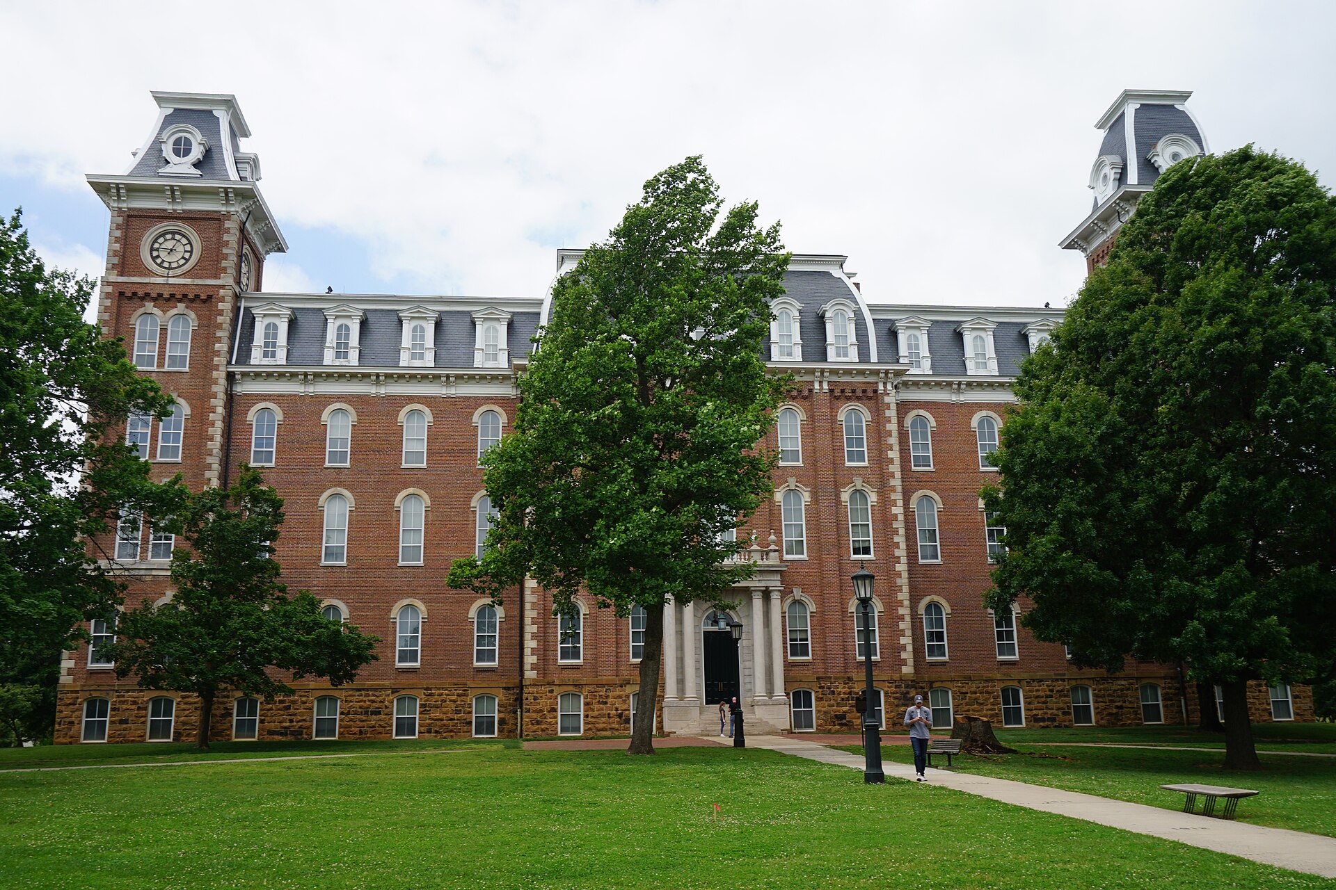 The red-brick Old Main at the University of Arkansas in Fayetteville, with its two towers rising above a green lawn.