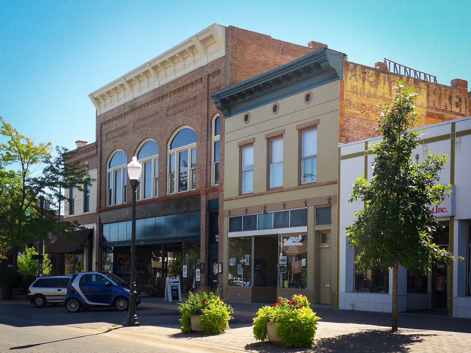 Historic brick storefronts with arched windows and a faded painted sign along 9th Street in downtown Greeley on a sunny day.