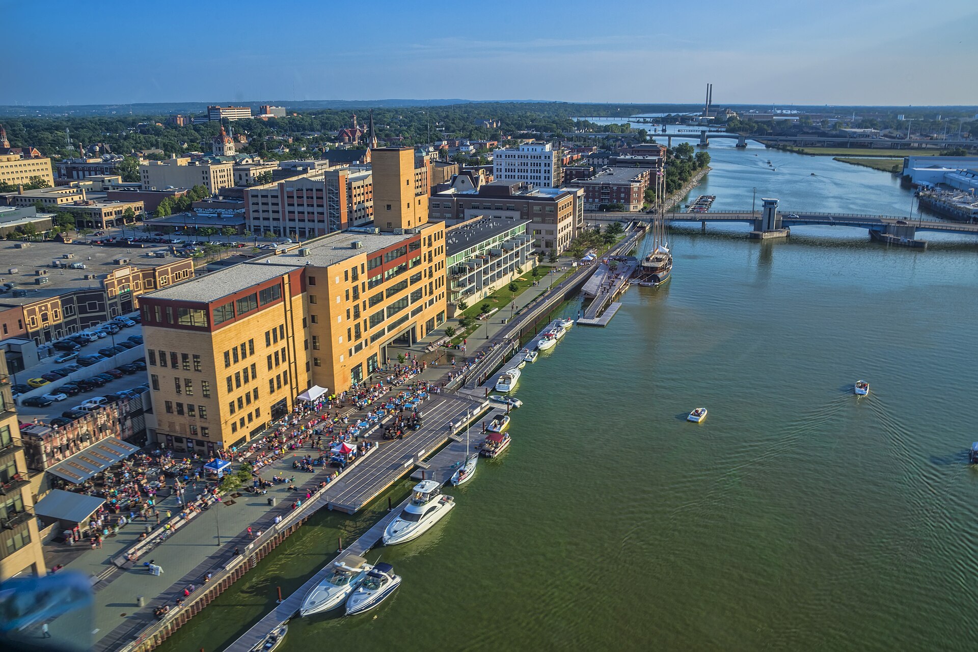 Downtown Green Bay's CityDeck and docked boats along the Fox River, seen from above on a sunny summer evening.