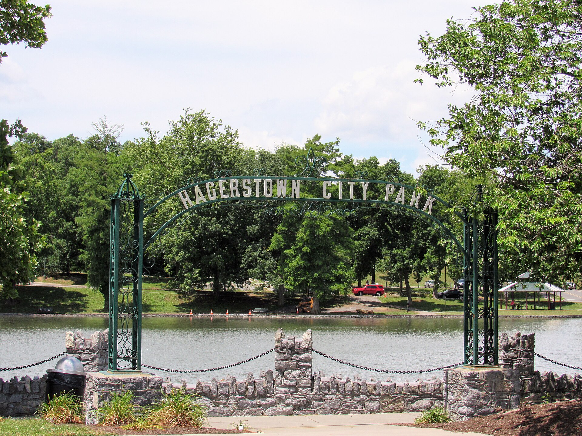 A green iron arch reading Hagerstown City Park stands before the park's lake and shade trees on a summer day.