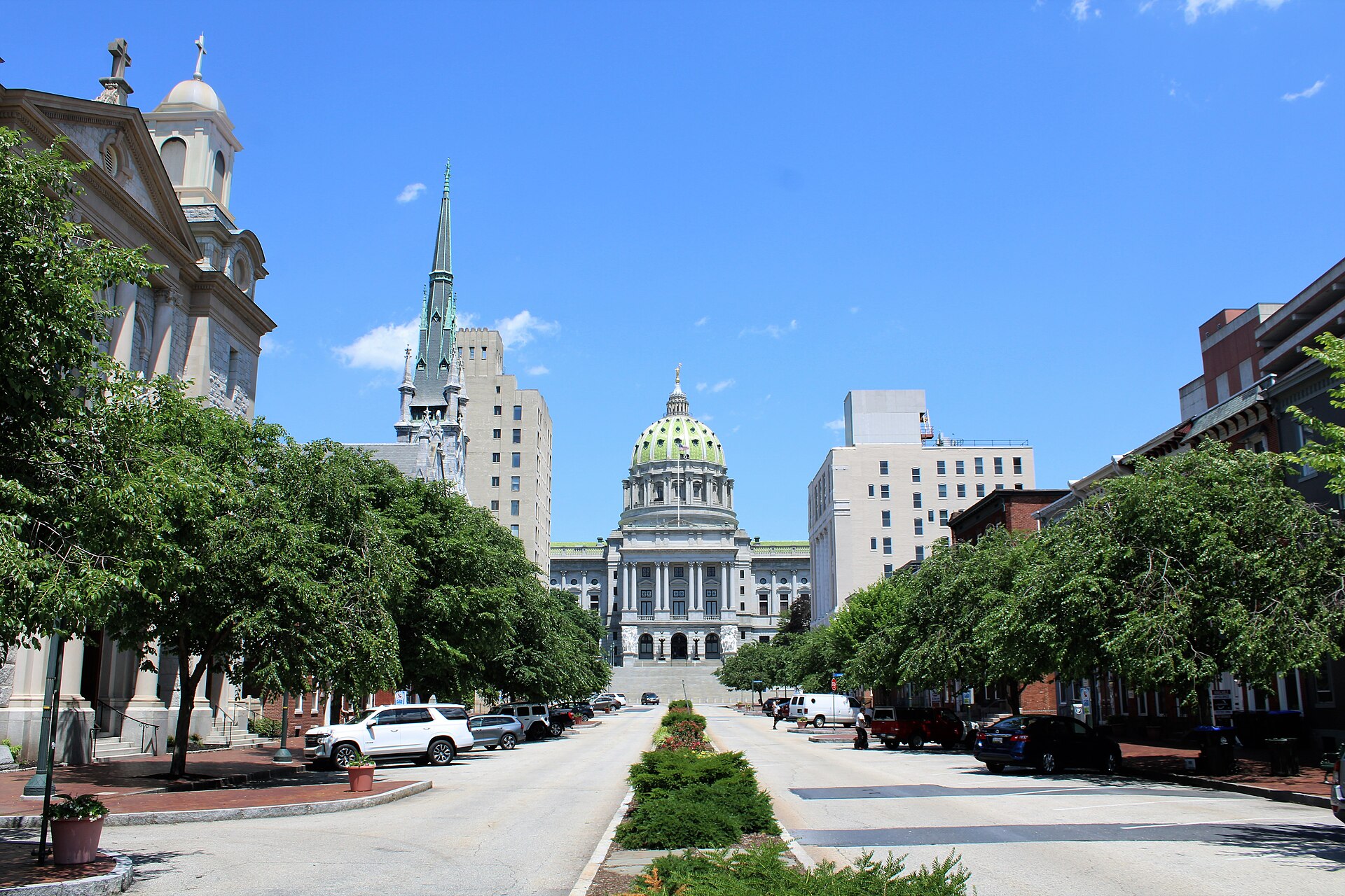 Tree-lined State Street leading to the green dome of the Pennsylvania State Capitol in Harrisburg under a clear blue sky.