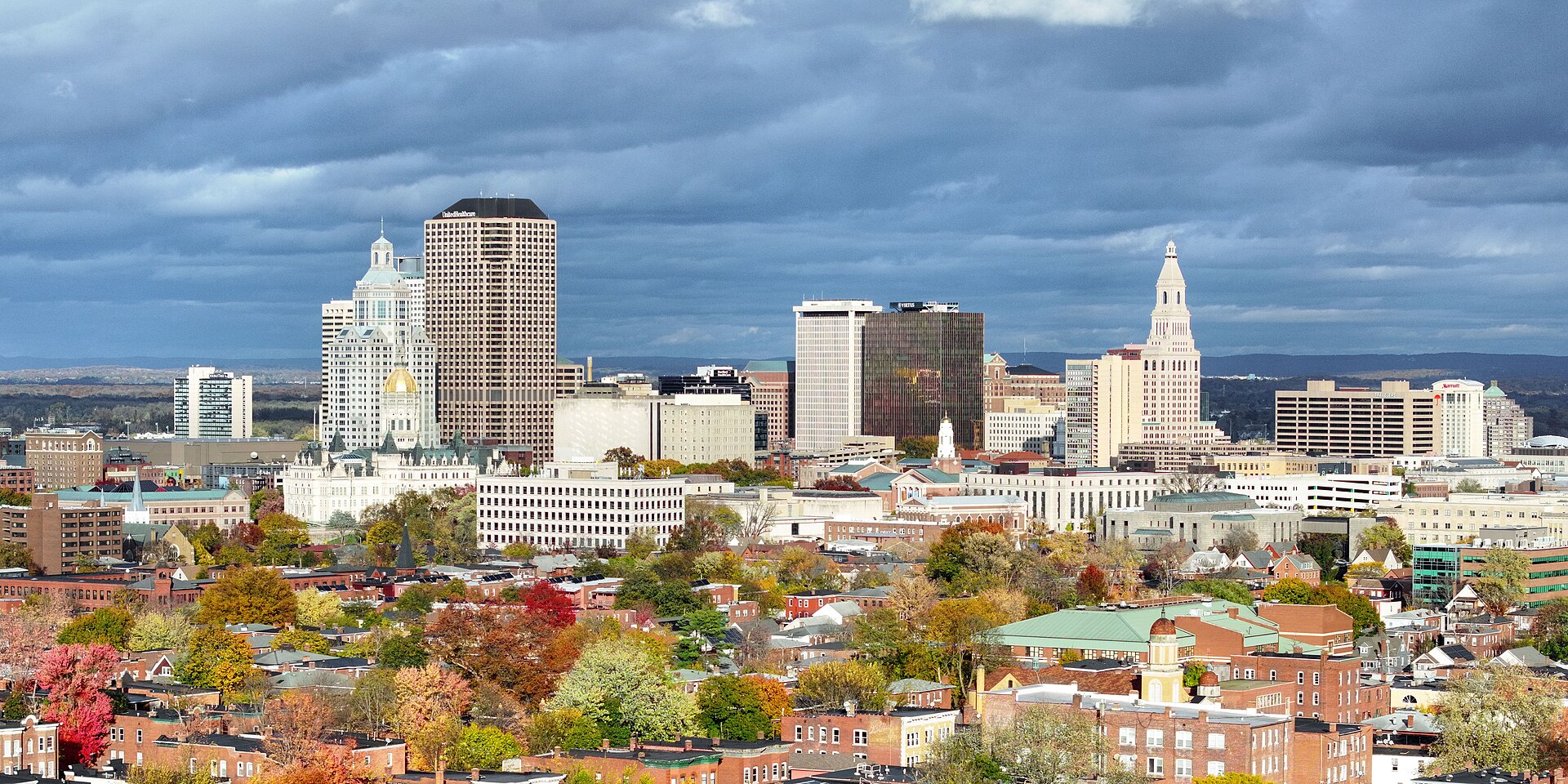 Hartford's skyline, with the gold-domed State Capitol and the Travelers Tower, rising above autumn trees under a stormy sky.