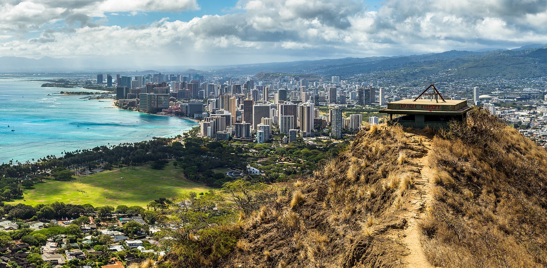 Waikiki high-rises and turquoise sea, with green parkland below, seen from the Diamond Head crater rim in Honolulu.