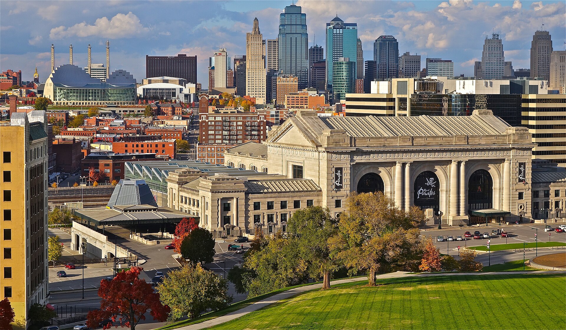 Kansas City's Union Station and downtown skyline in golden autumn light, with fall trees and a green lawn in front.