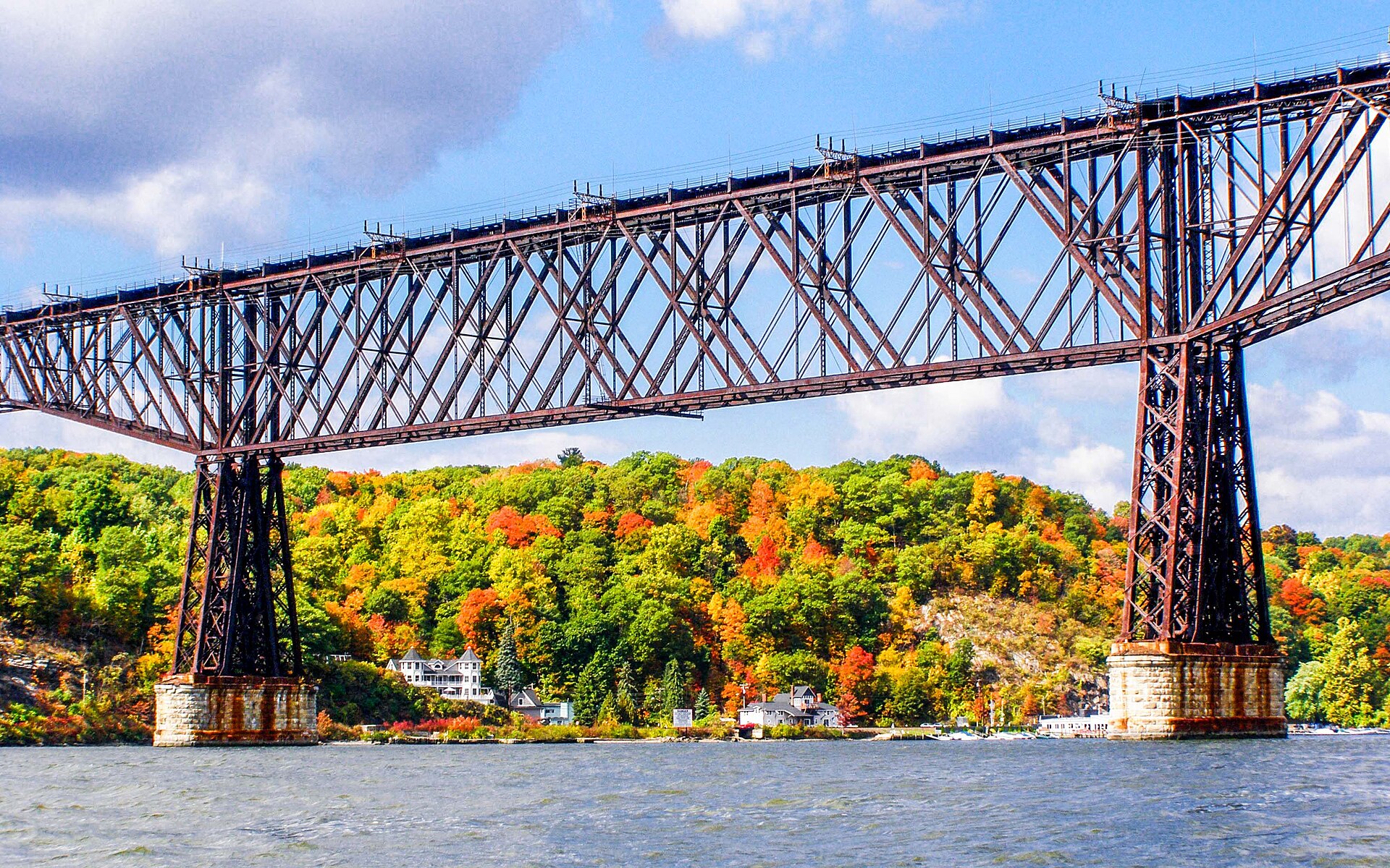 The steel trusses of the Walkway Over the Hudson at Poughkeepsie tower over the river beneath autumn-coloured hills.