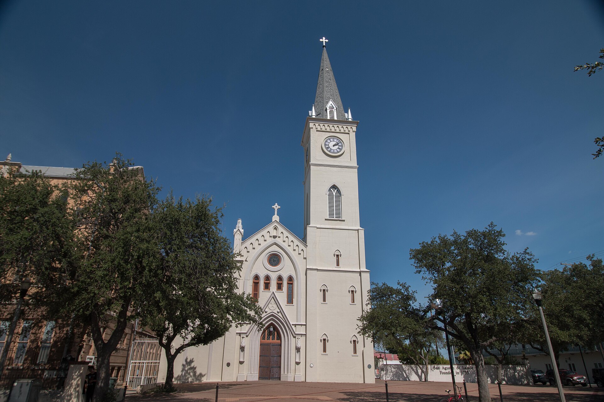 The white San Agustín Cathedral and its clock tower rising above the plaza’s trees in Laredo’s historic district under a deep blue sky.