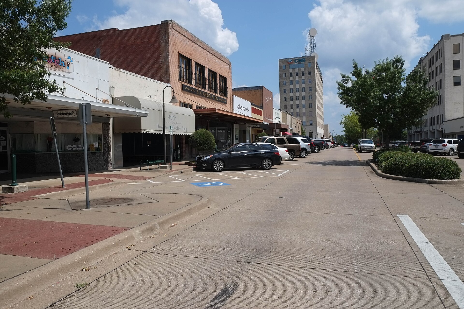 Brick storefronts and mid-rise towers along a quiet street in downtown Longview, Texas, on a sunny day.