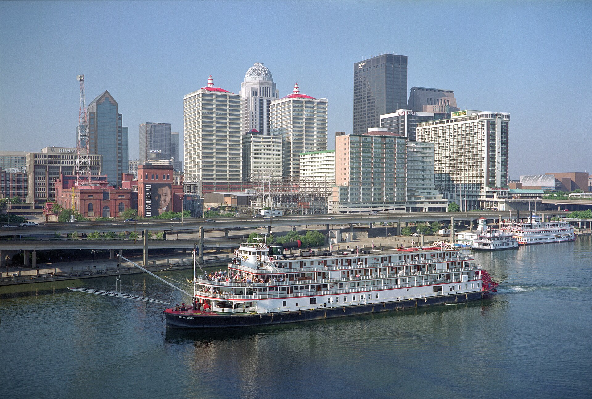 The paddle steamboat Delta Queen cruises the Ohio River below downtown Louisville's towers on a clear day.