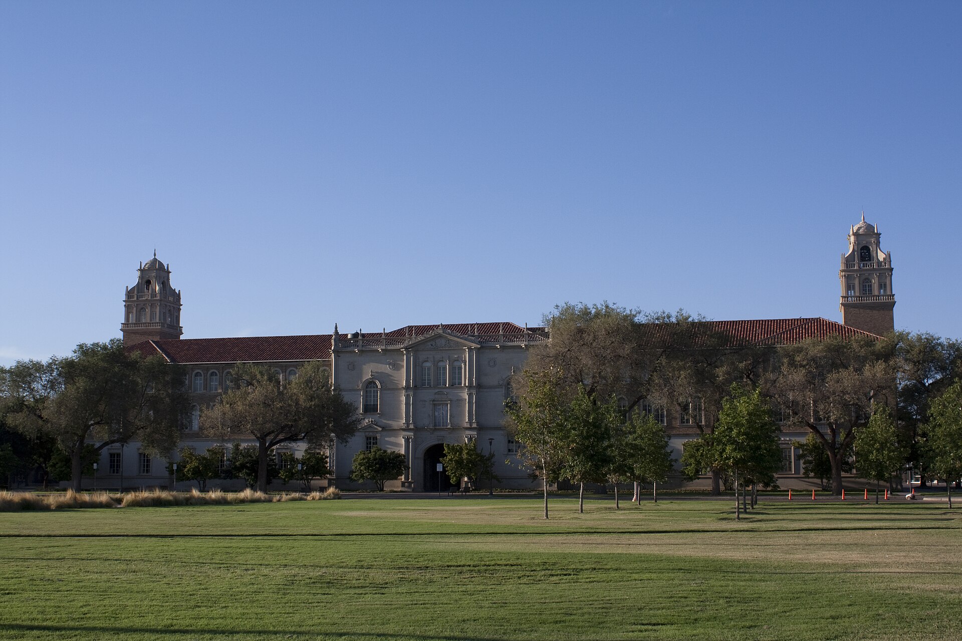 Texas Tech University's Administration Building in Lubbock, with its two bell towers, beyond a wide lawn under a clear sky.