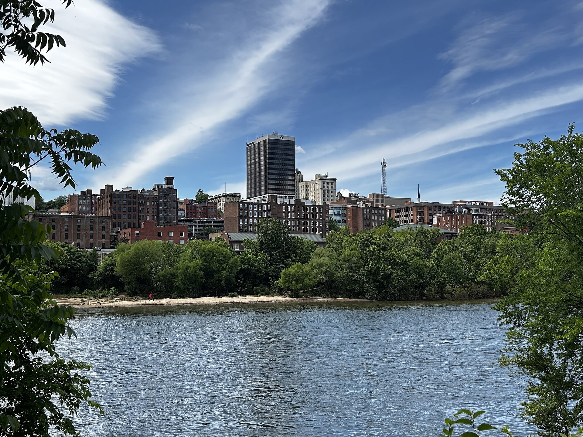 Downtown Lynchburg's brick buildings and tower rising above the tree-lined James River under a blue, streaky sky.
