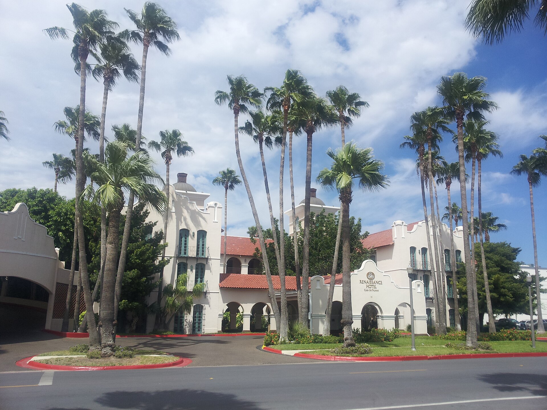 Tall palm trees in front of the white Spanish-style Casa de Palmas hotel in downtown McAllen under a blue sky.