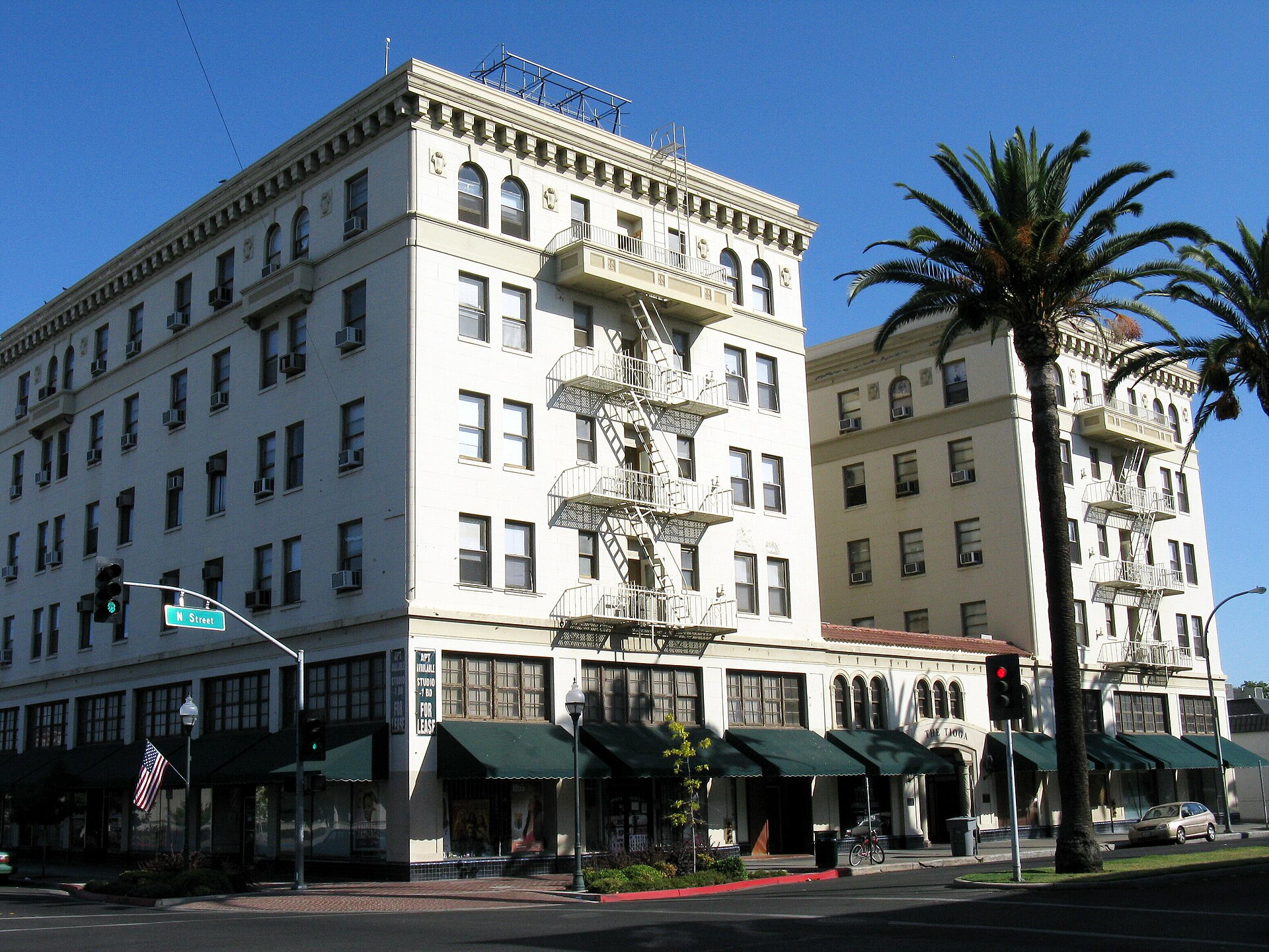The white historic Tioga Hotel with tall palm trees on a sunny day in downtown Merced.