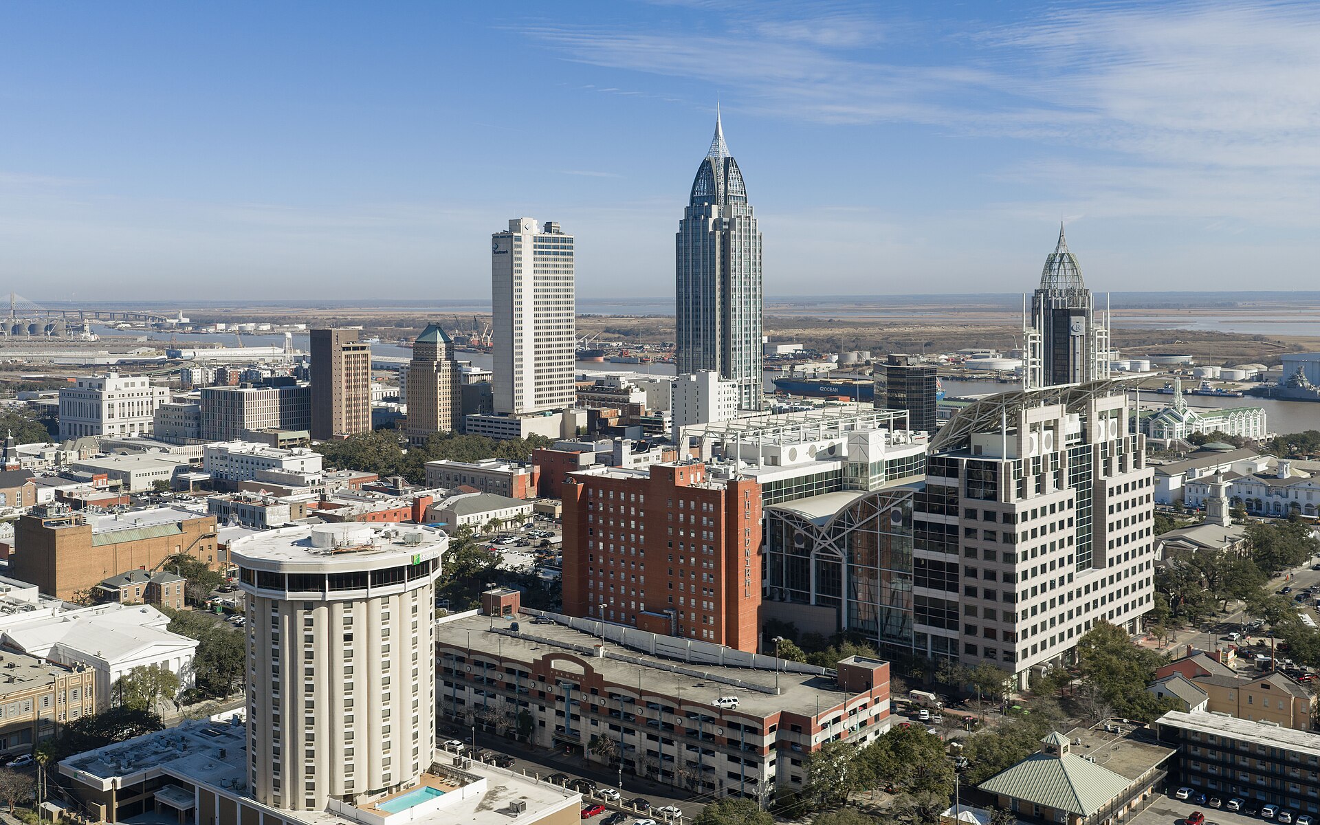 Downtown Mobile's skyline, led by the spired RSA Battle House Tower, under a clear blue sky.