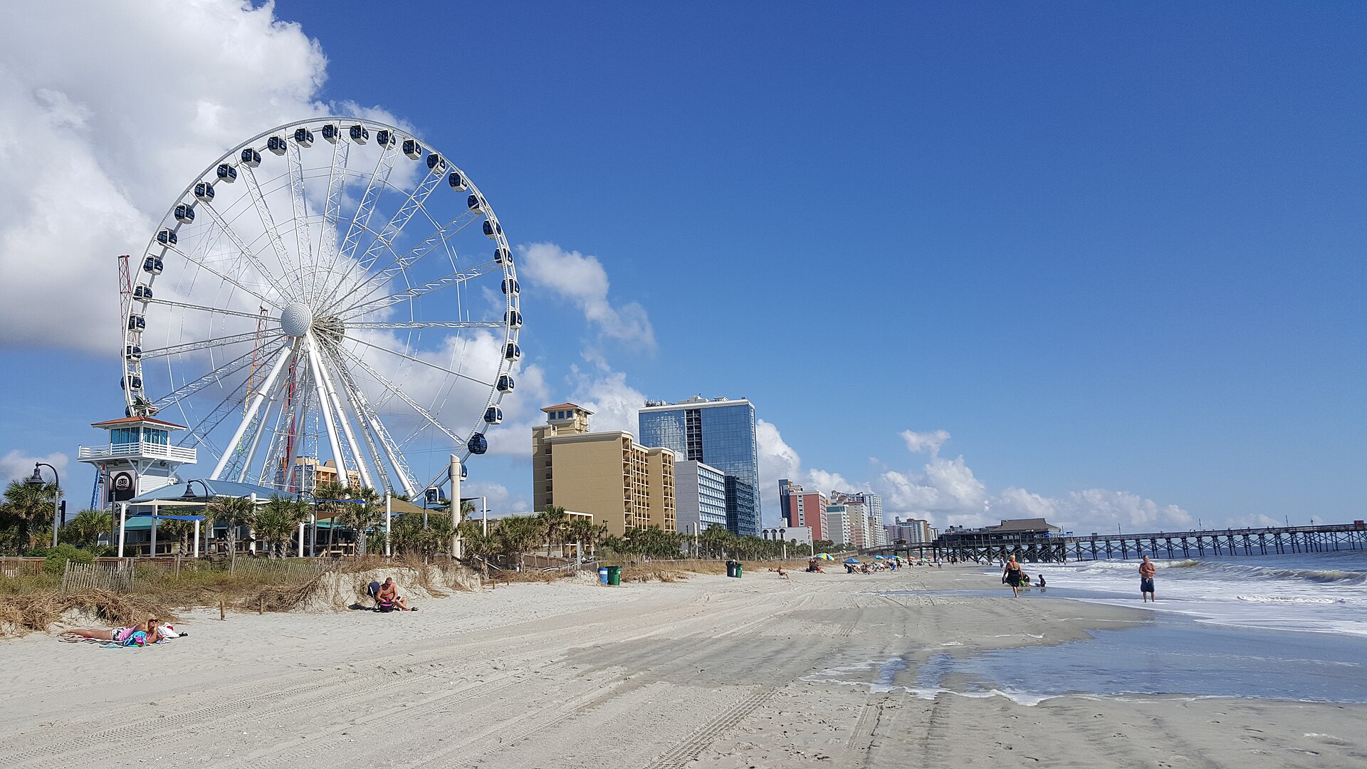 The SkyWheel and oceanfront hotels above the wide sandy beach at Myrtle Beach on a sunny day.