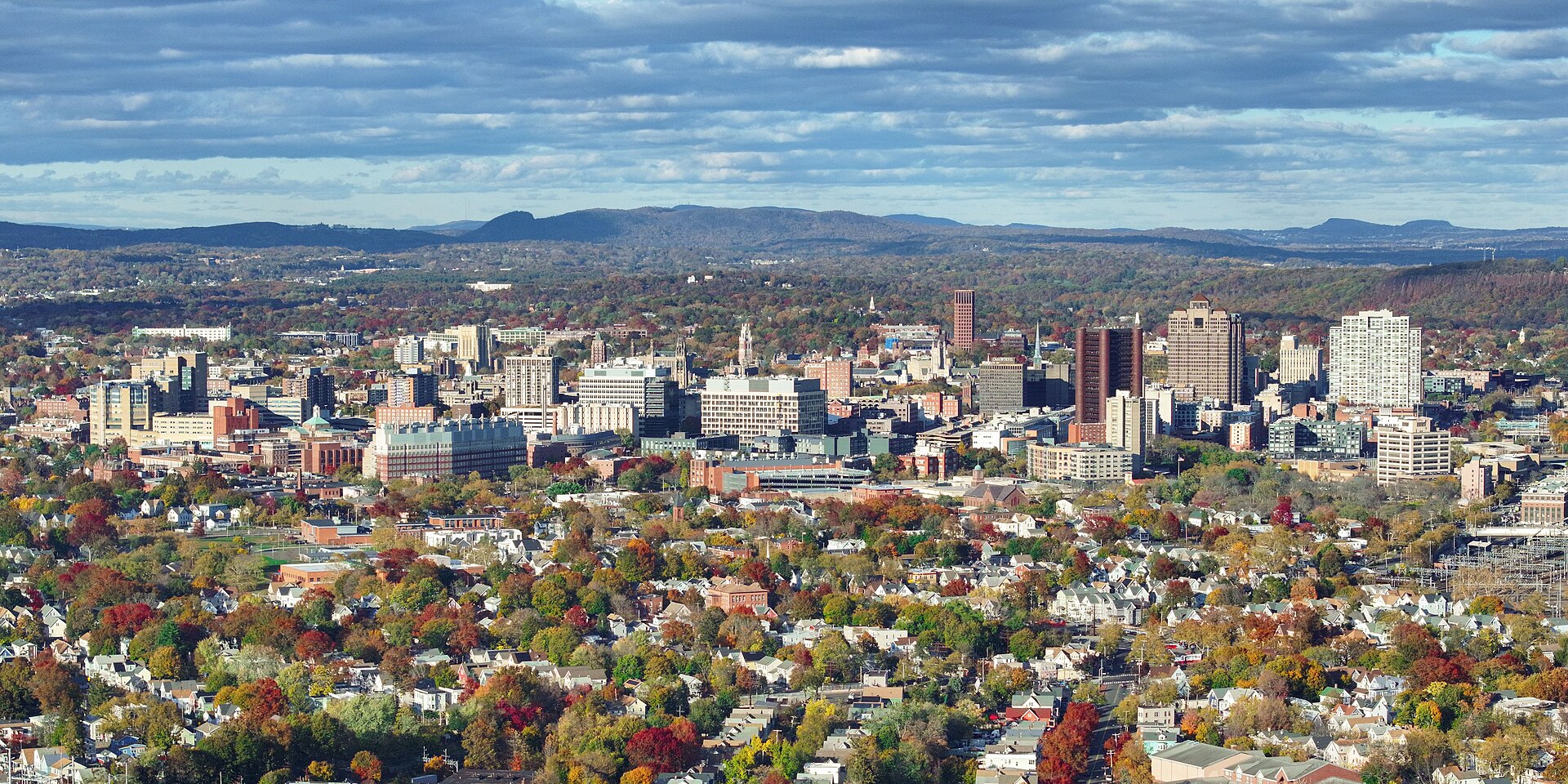 Downtown New Haven's towers rising above tree-filled neighborhoods in autumn color, with low hills on the horizon.
