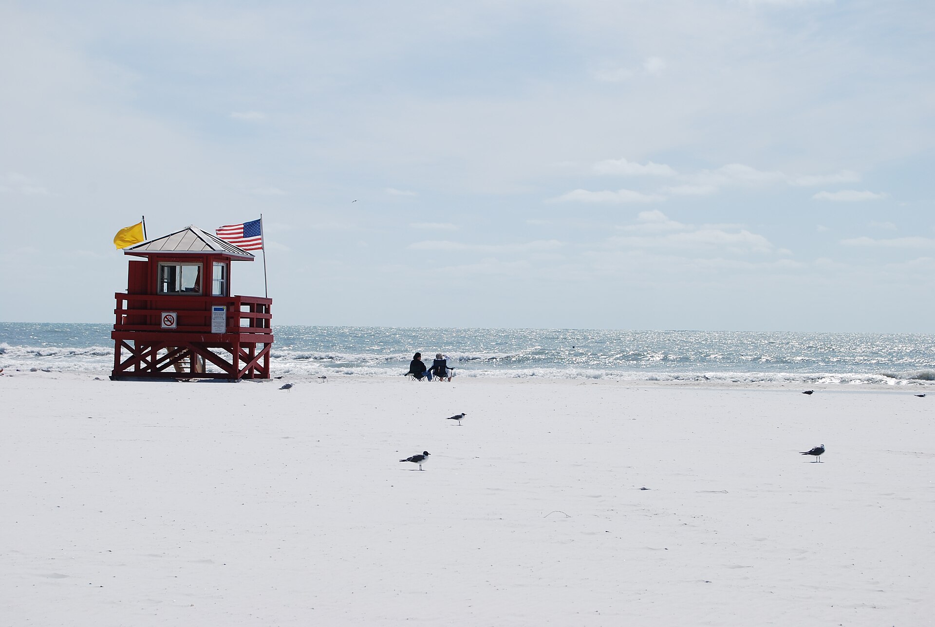 A red lifeguard stand on the white quartz sand of Siesta Key Beach by calm Gulf waters near Sarasota.