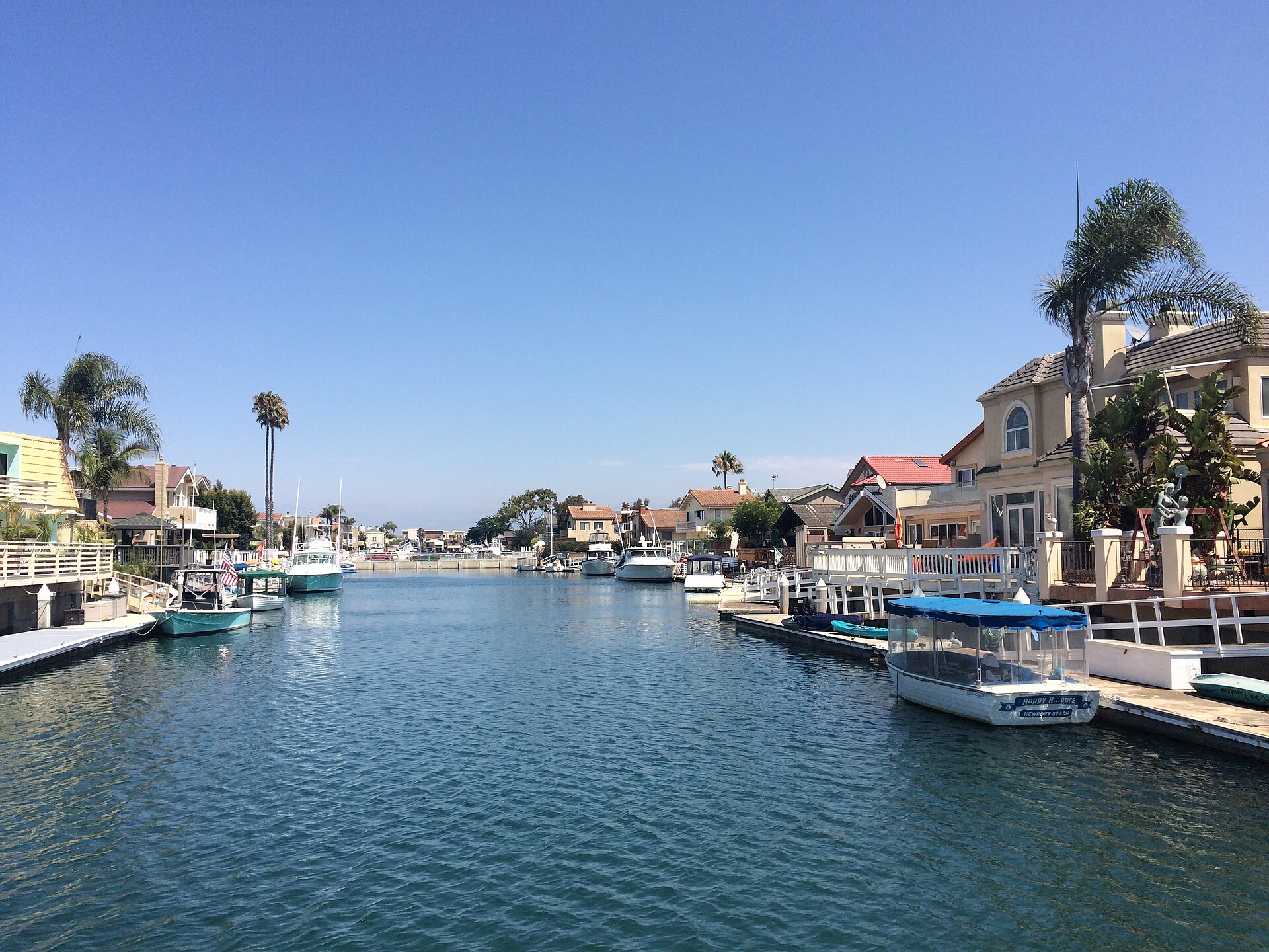 Boats moored along a palm-lined residential canal at Channel Islands Harbor in Oxnard on a sunny day.