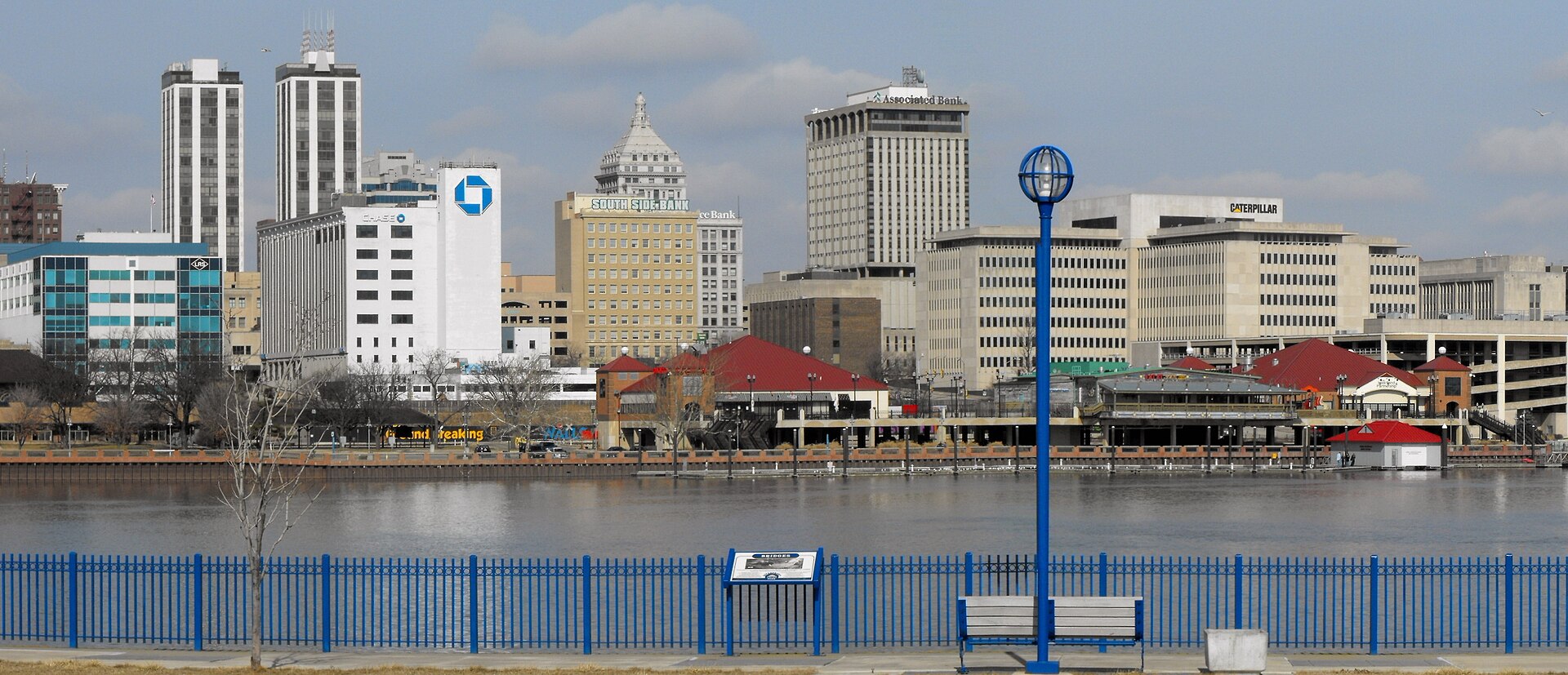Downtown Peoria’s towers across the Illinois River, seen from the East Peoria riverfront with its blue railing on a winter day.