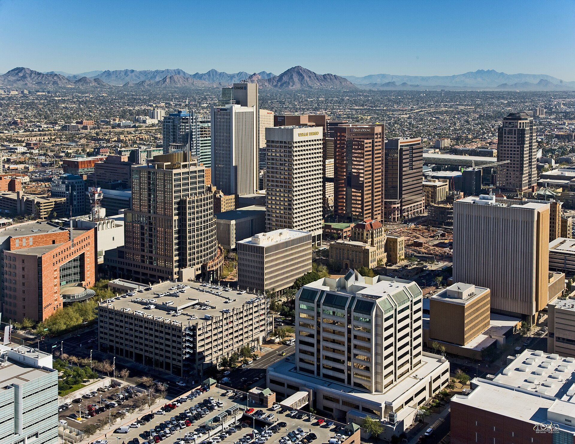 Downtown Phoenix high-rises with desert mountains on the horizon, seen from the air on a clear, sunny day.