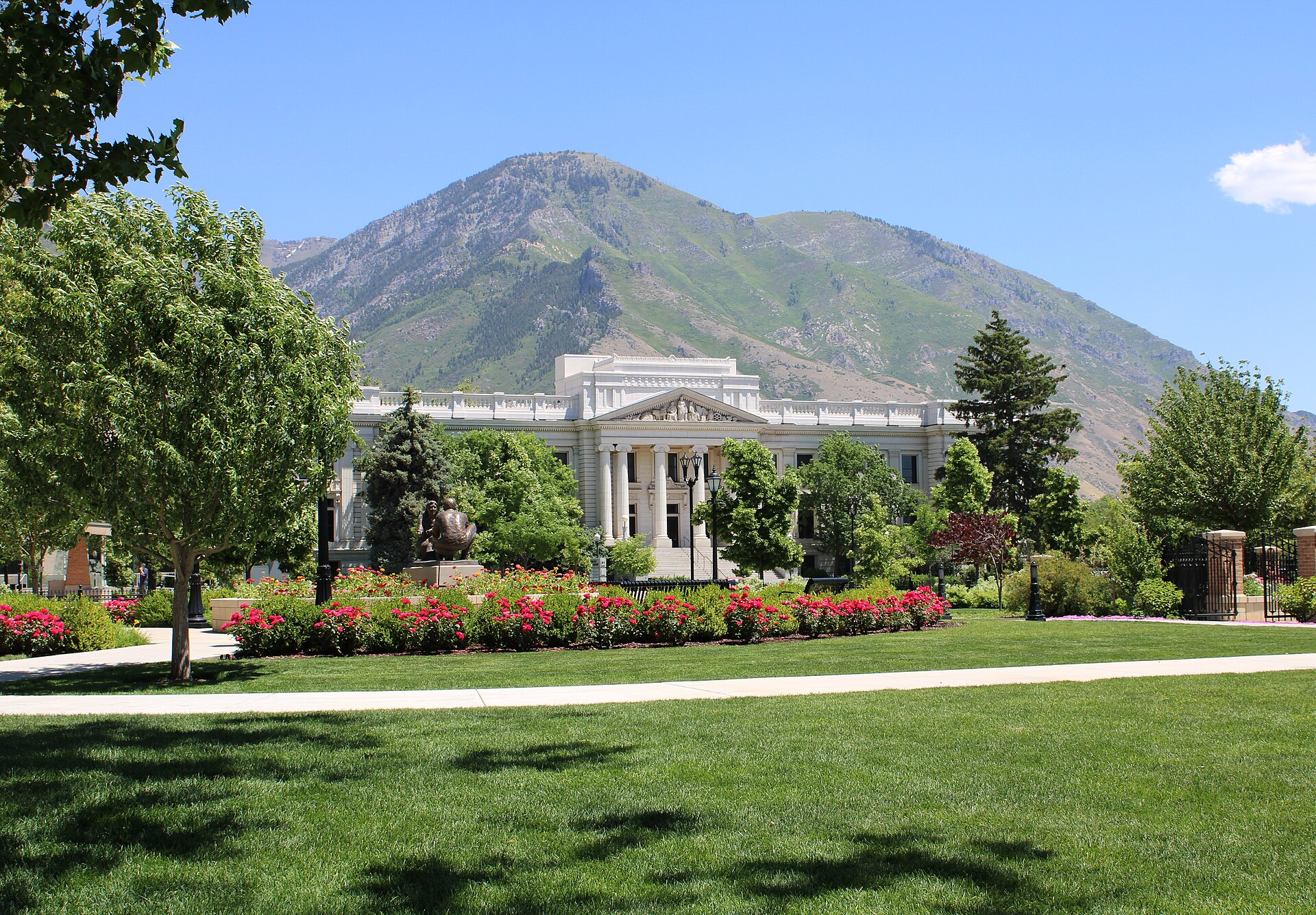 The white-columned Historic Utah County Courthouse behind lawns and red flower beds, with a green Wasatch peak rising behind.