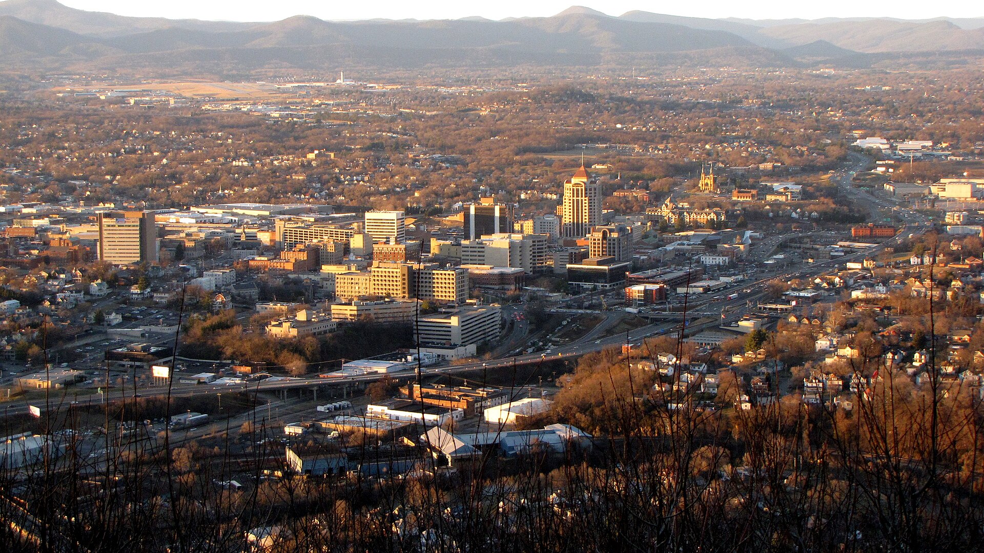 Downtown Roanoke from Mill Mountain in late-afternoon sun, with Blue Ridge ridges on the horizon.