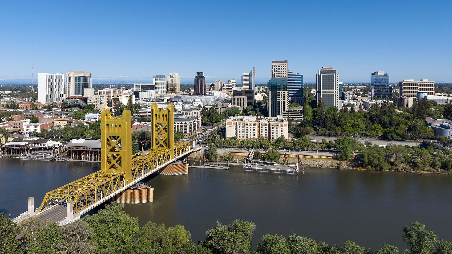 The gold Tower Bridge over the Sacramento River with downtown Sacramento's skyline behind on a sunny day.