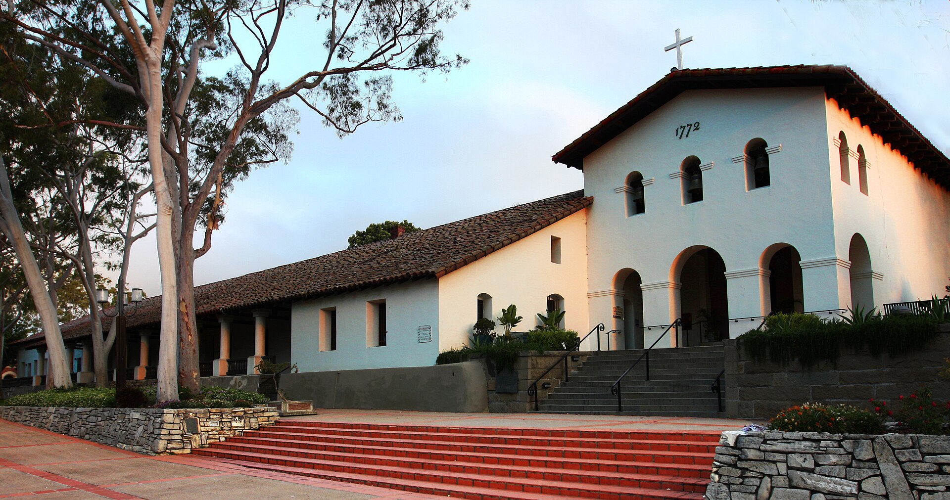 The white adobe church and bell wall of Mission San Luis Obispo de Tolosa in warm evening light.