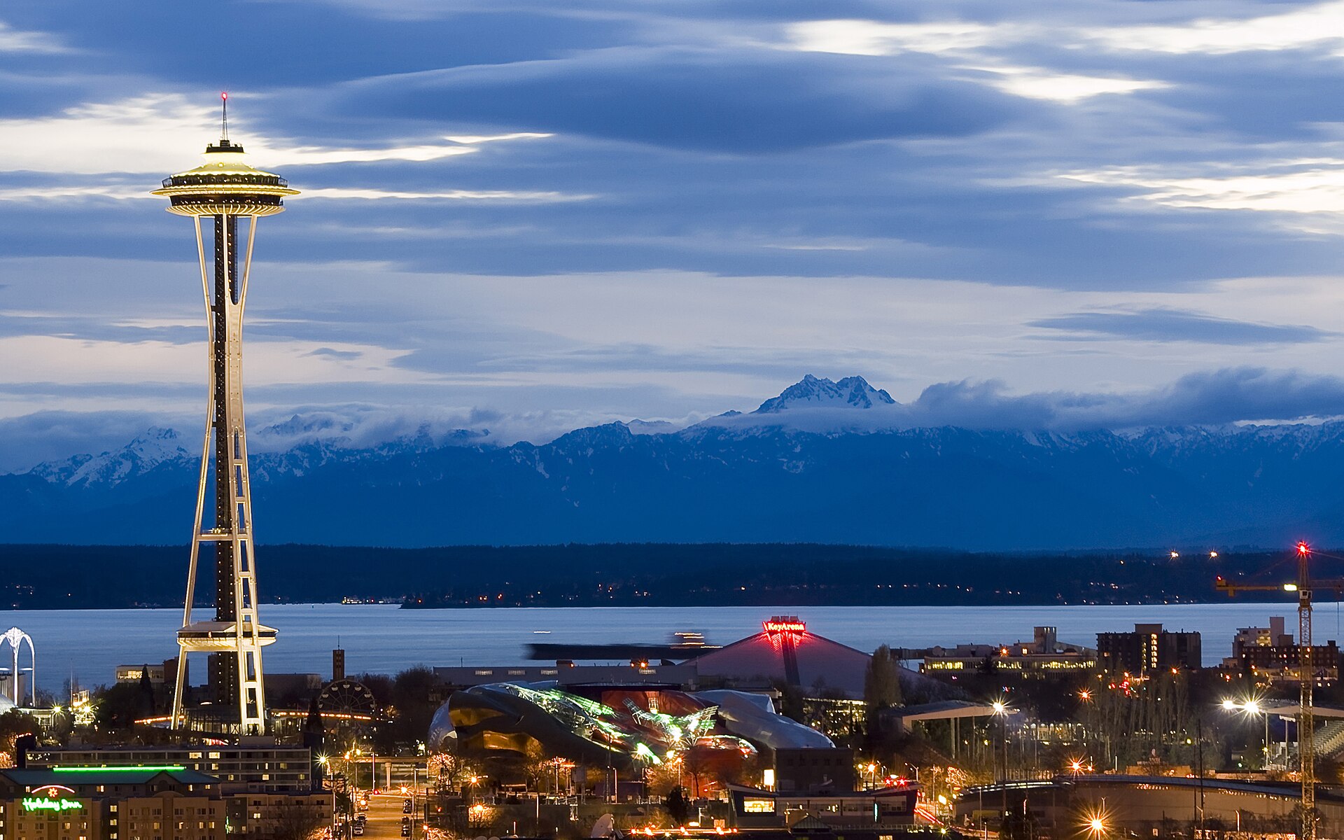 The Space Needle against the Olympic Mountains and Elliott Bay as night falls in Seattle.