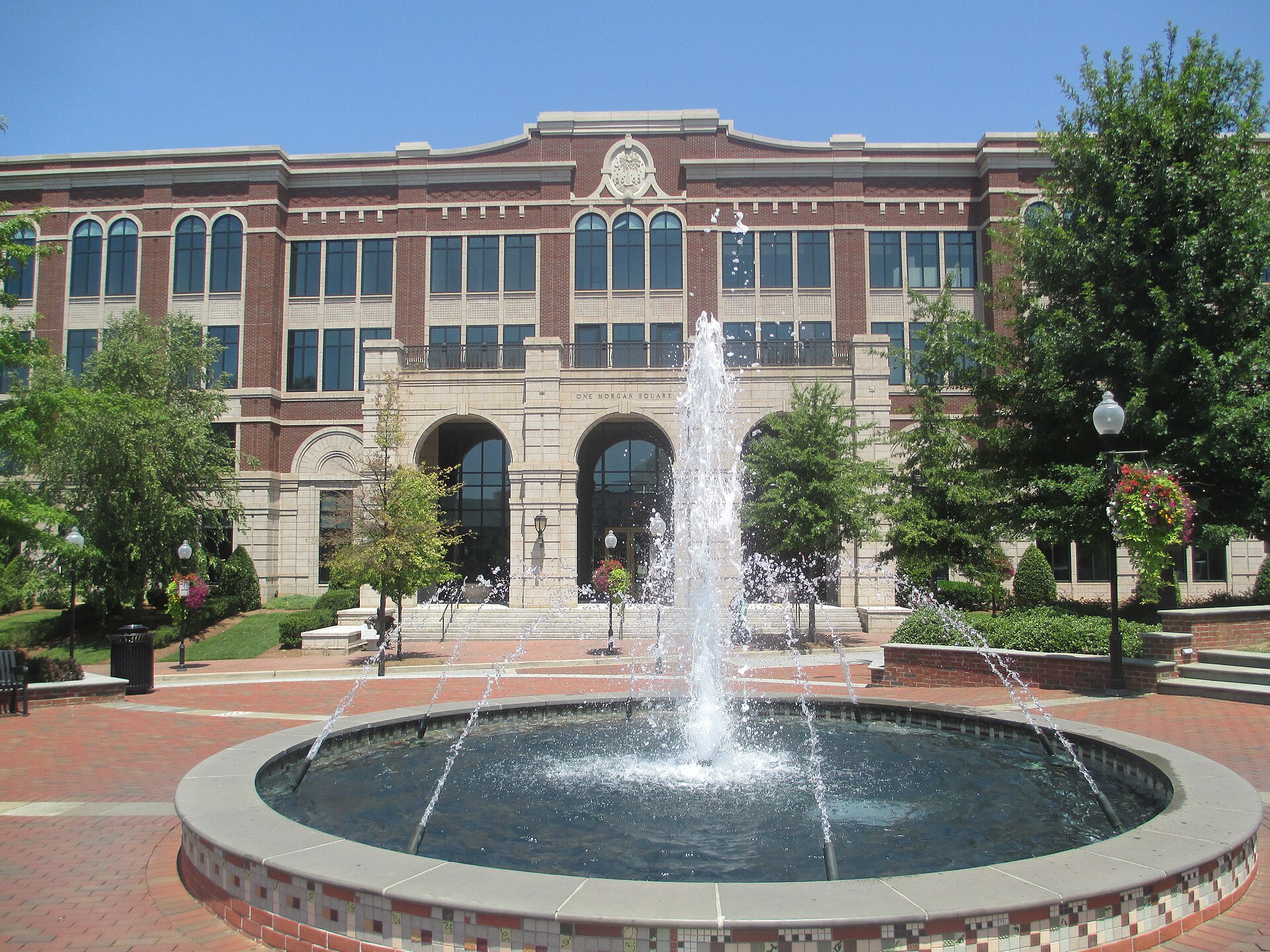 The fountain on Morgan Square in downtown Spartanburg, in front of the arched brick and stone One Morgan Square building on a sunny day.