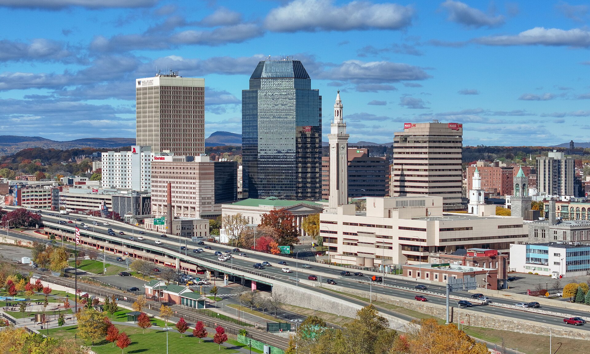 Downtown Springfield's towers and Campanile above autumn trees under a blue sky with white clouds.
