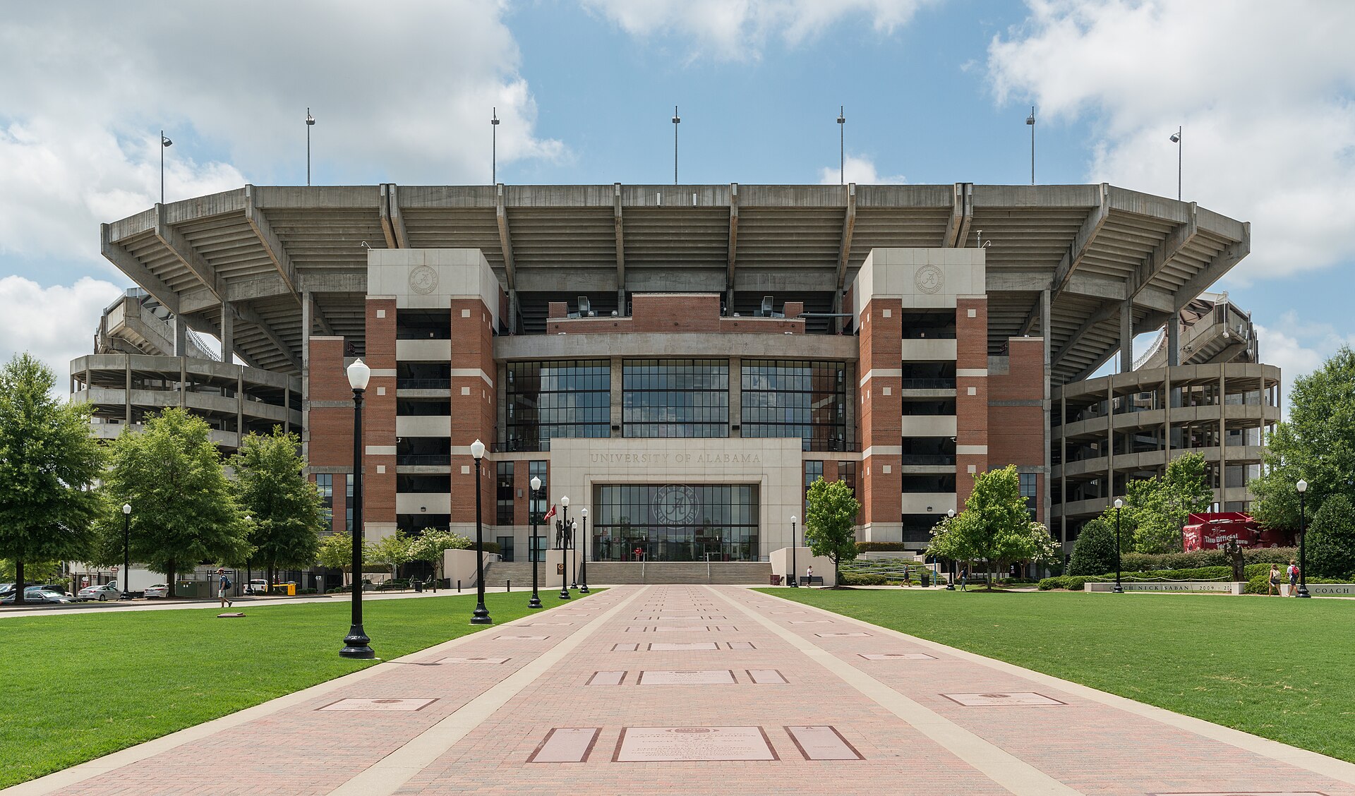 The brick and concrete north facade of Bryant-Denny Stadium at the end of a wide brick walkway on a sunny day in Tuscaloosa.
