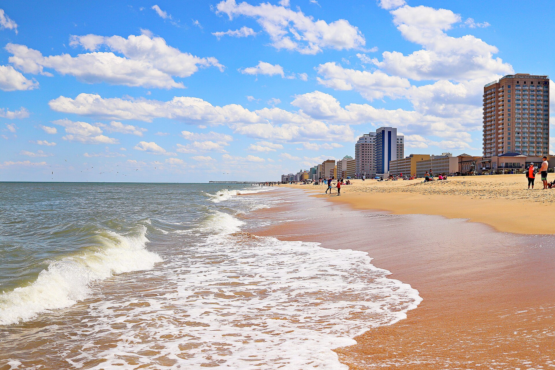 Waves rolling onto the wide sandy beach at the Virginia Beach Oceanfront, with hotels lining the shore.