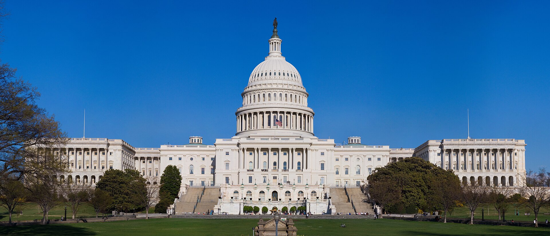 The white-domed United States Capitol in Washington, D.C., seen across its west lawn under a clear blue sky.